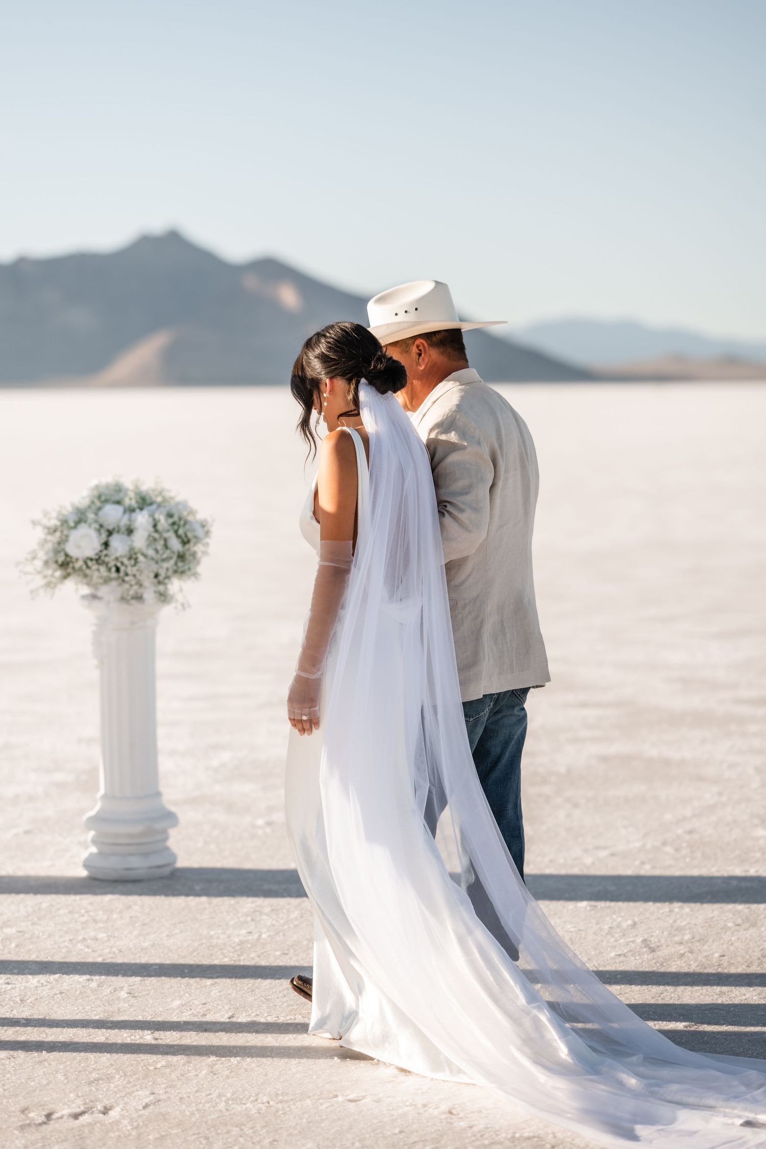 A romantic wedding ceremony setup on a salt flat with white floral arrangements and flowing veil.