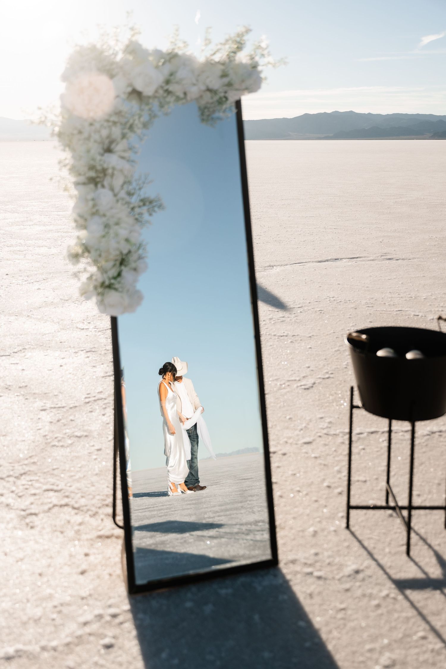 Wedding ceremony setup on salt flats with white floral arrangements and black chairs.