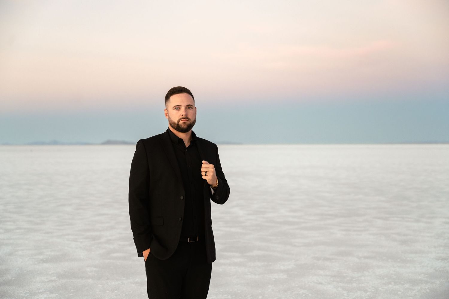 Groom in black suit poses emotionally on salt flats at sunset.