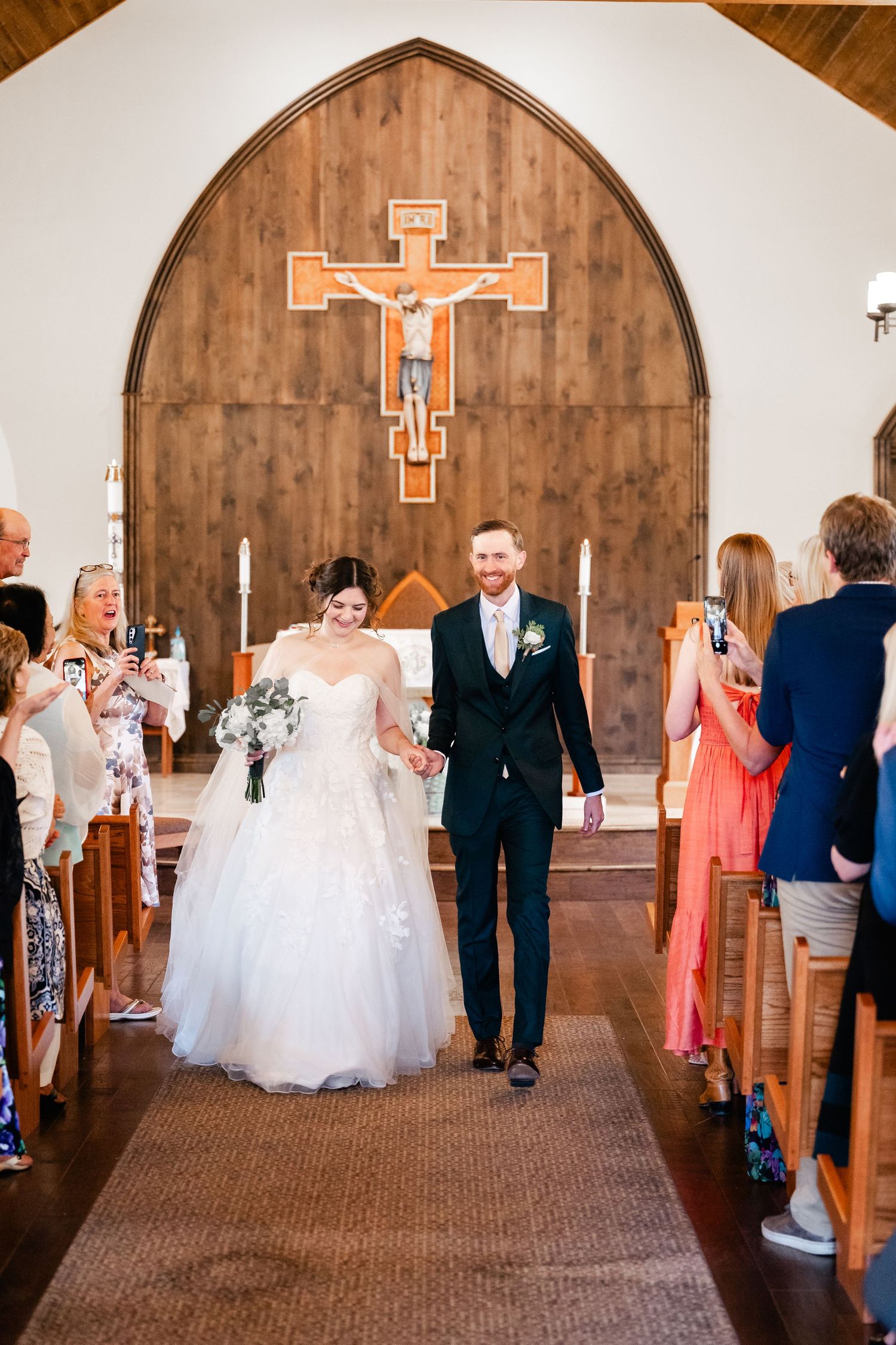 Wedding ceremony processional in church sanctuary with wooden arch and cross on altar.