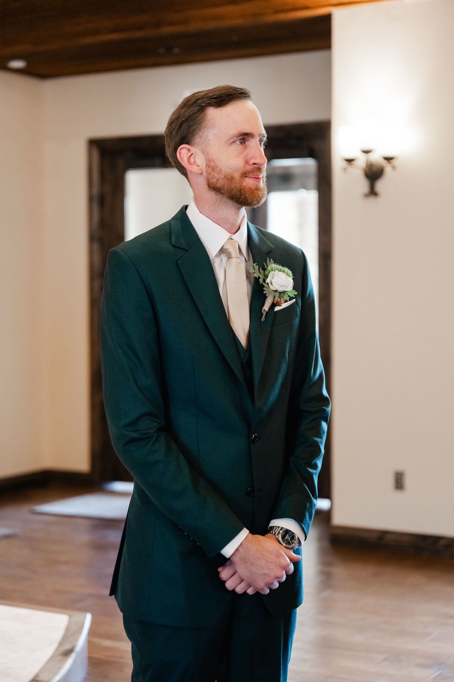 A groom in a dark suit and tie stands in anticipation during a wedding ceremony.