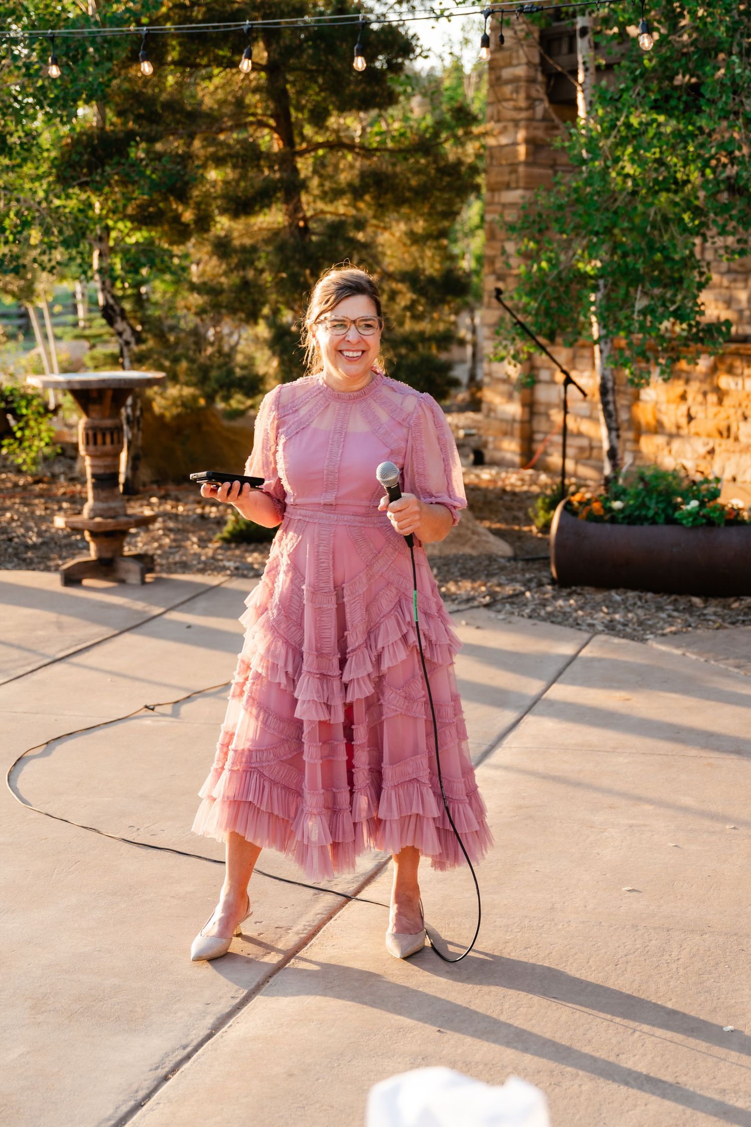 A person in a pink ruffled dress twirls on a concrete patio during golden hour.