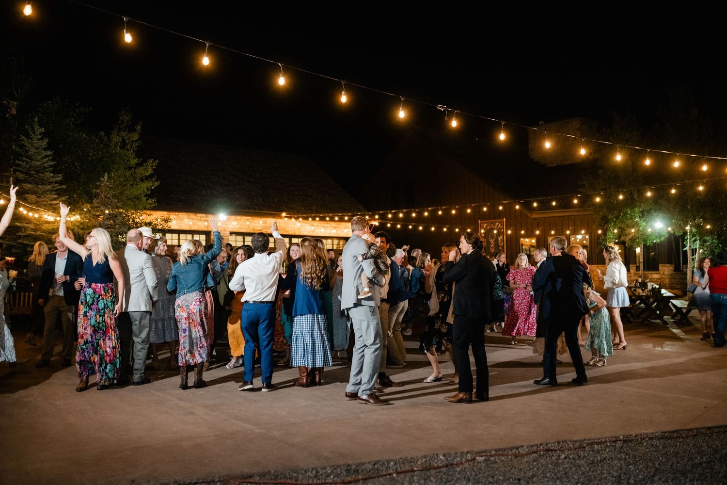 Wedding guests gather under string lights for an outdoor evening celebration.