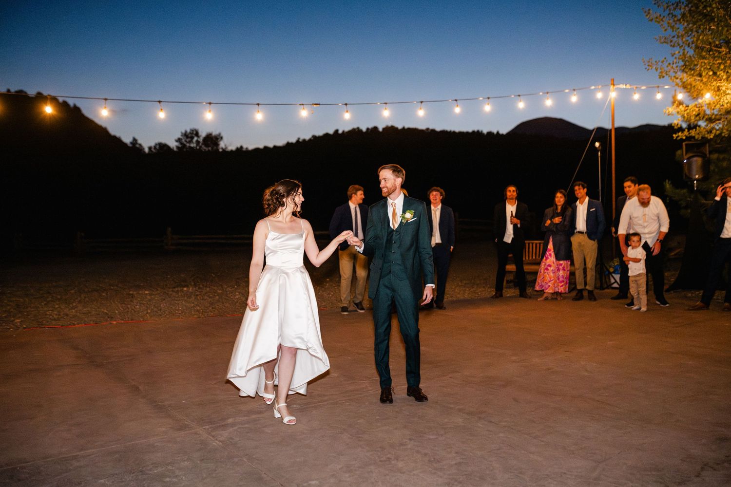 Couples dancing under string lights at an outdoor evening reception.