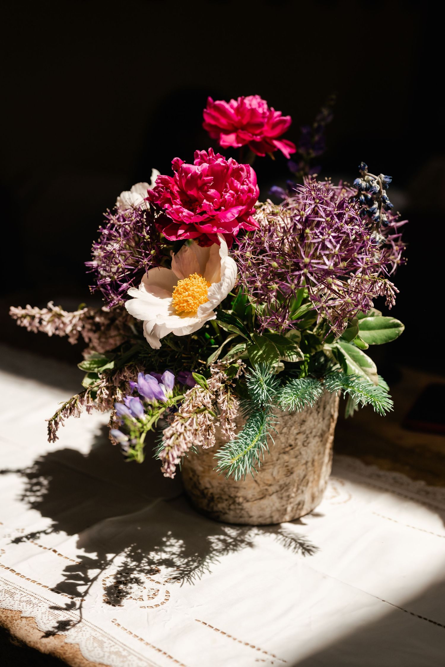 Floral centerpiece with pink roses and wildflowers in rustic stone container under dramatic lighting.