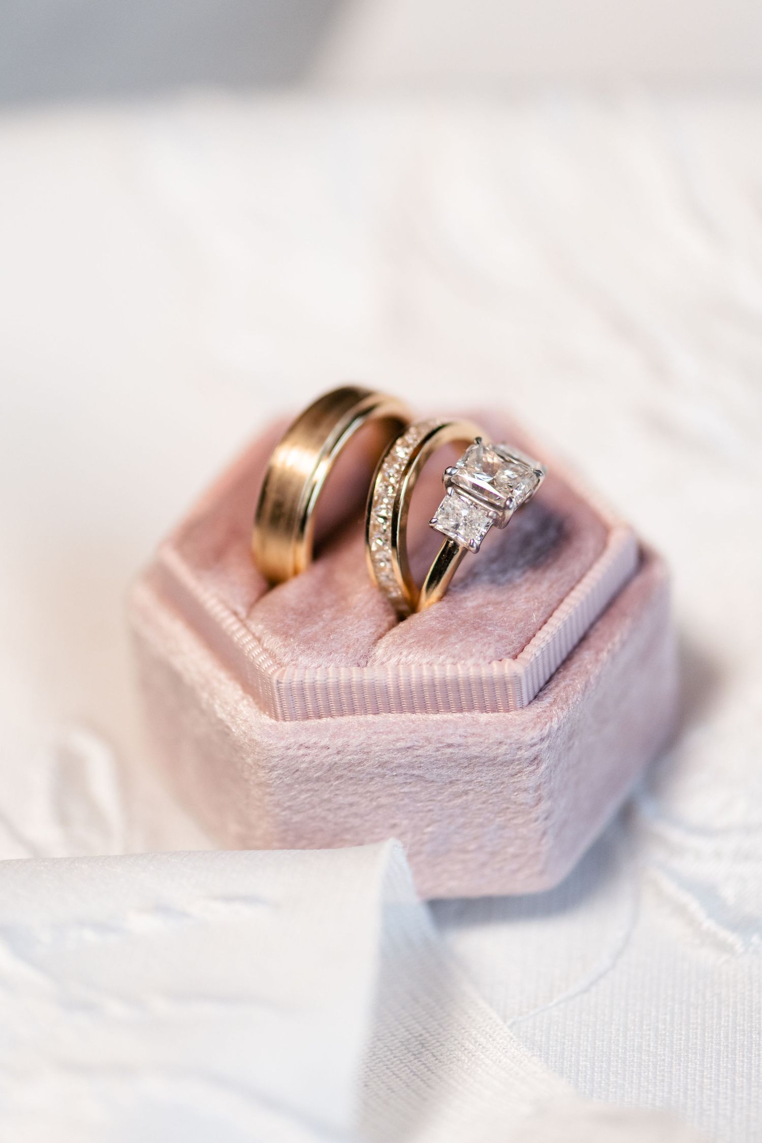 Wedding rings displayed on a pink hexagonal ring box with soft lighting.