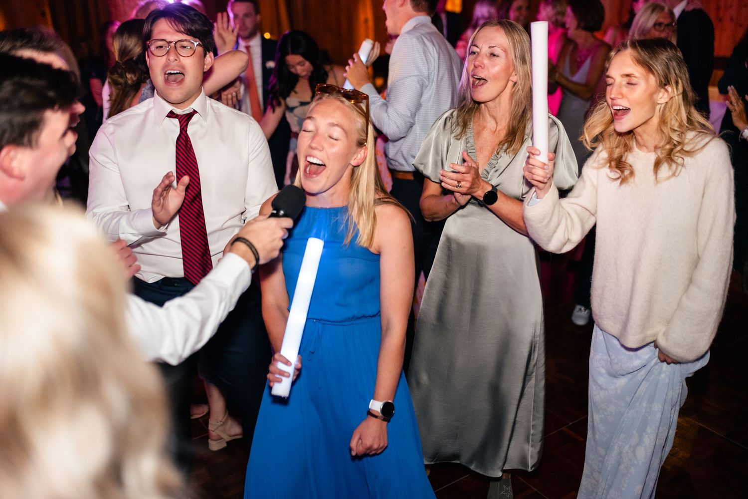 Wedding guests dancing and celebrating on foggy dance floor with colorful lighting.