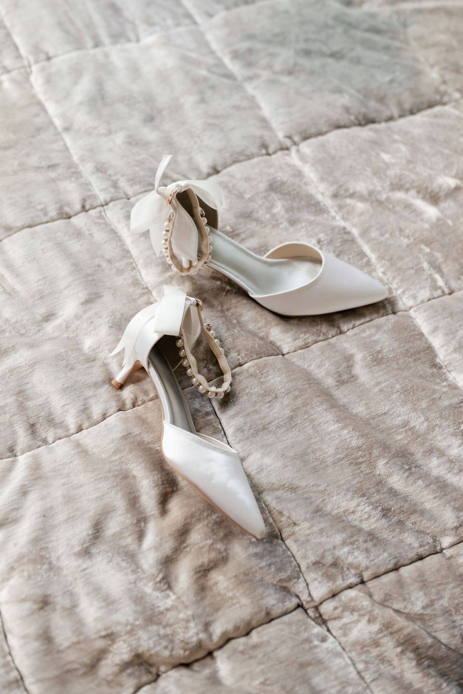 Elegant white bridal heels displayed on textured fabric background.
