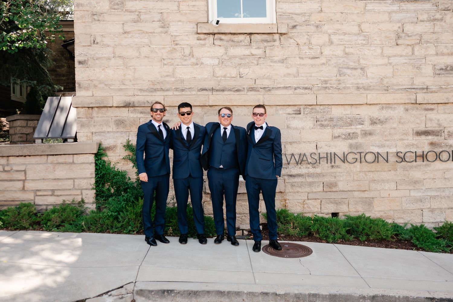 Group in formal attire standing against stone wall of Washington School building.