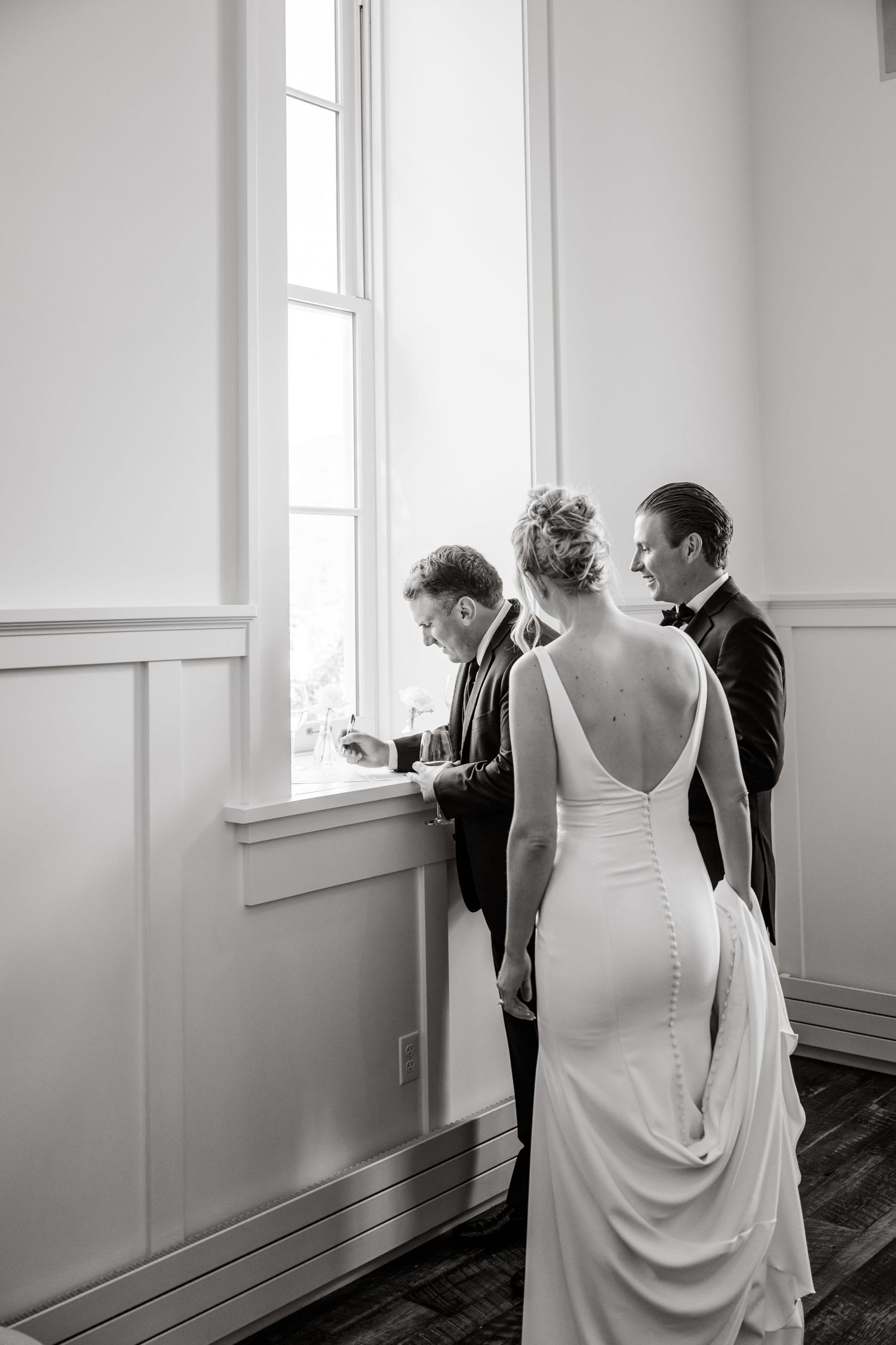 Wedding preparation sequence in black and white showing dress adjustments in a bright interior room.