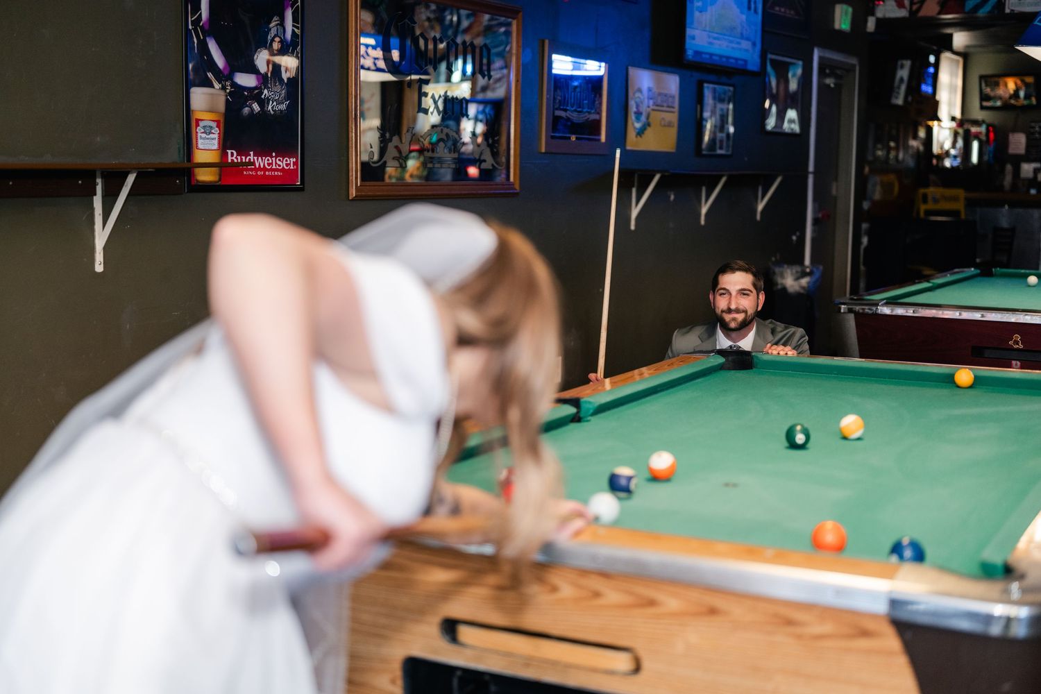 Two people lean in close together over a pool table in a dark bar setting.