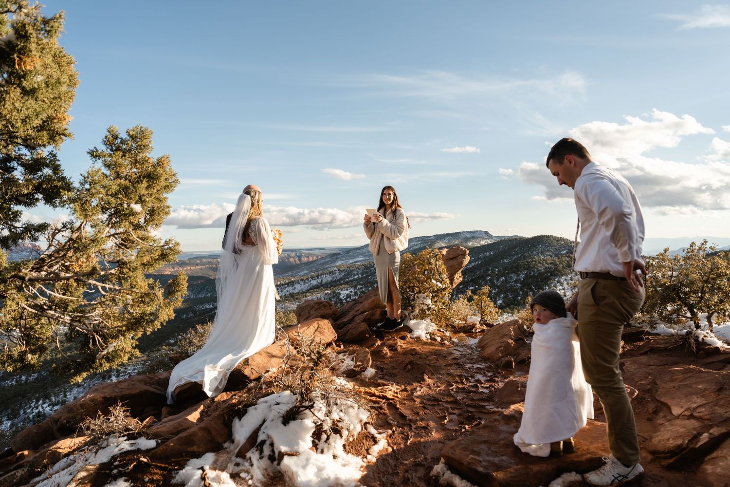 Wedding party gathered on rocky mountain overlook during sunset.