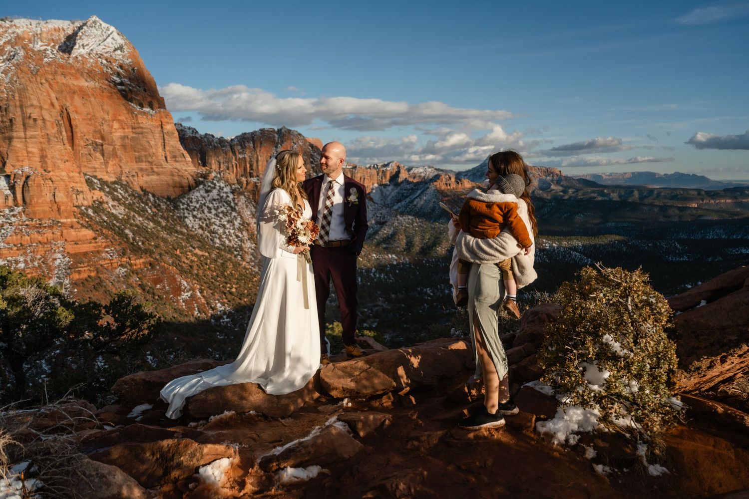 Panoramic wedding photography session on red rock cliffs with expansive mountain views.
