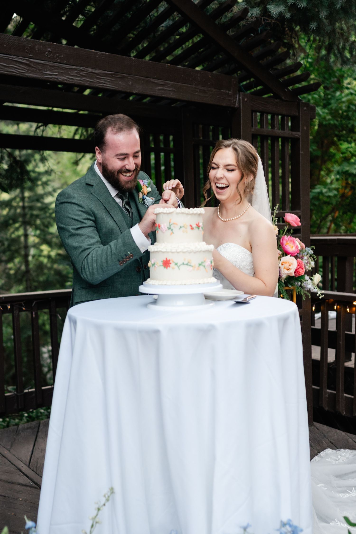 Couple sharing cake at their wedding reception under a wooden pavilion with white tablecloth. Millcreek Inn Wedding Photographer.