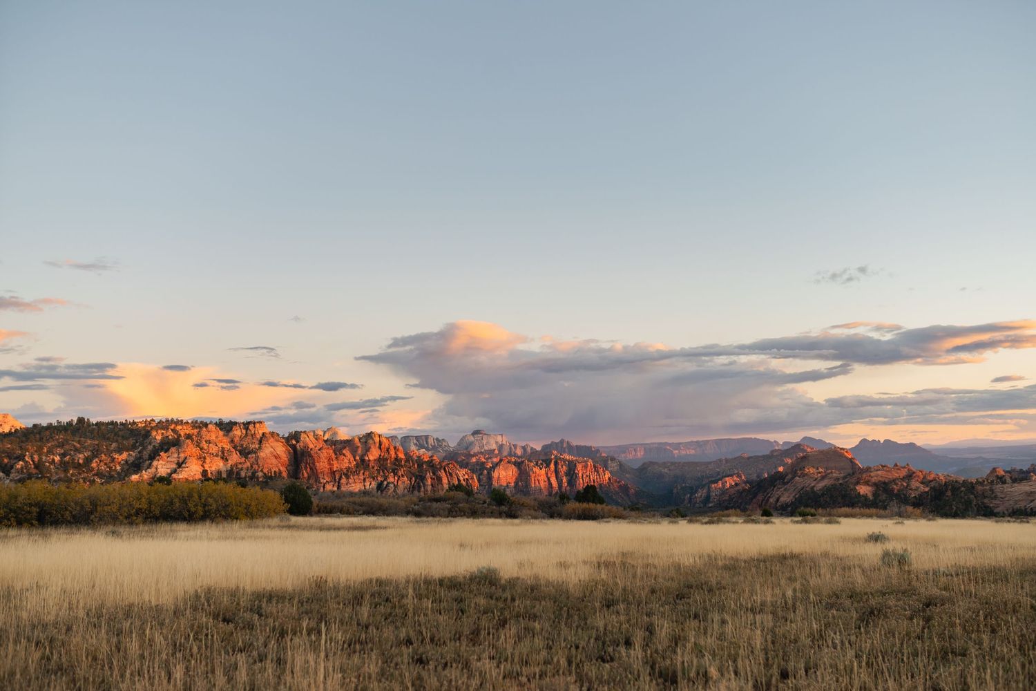 Wide landscape panorama of mountains and fields at sunset with warm golden light.