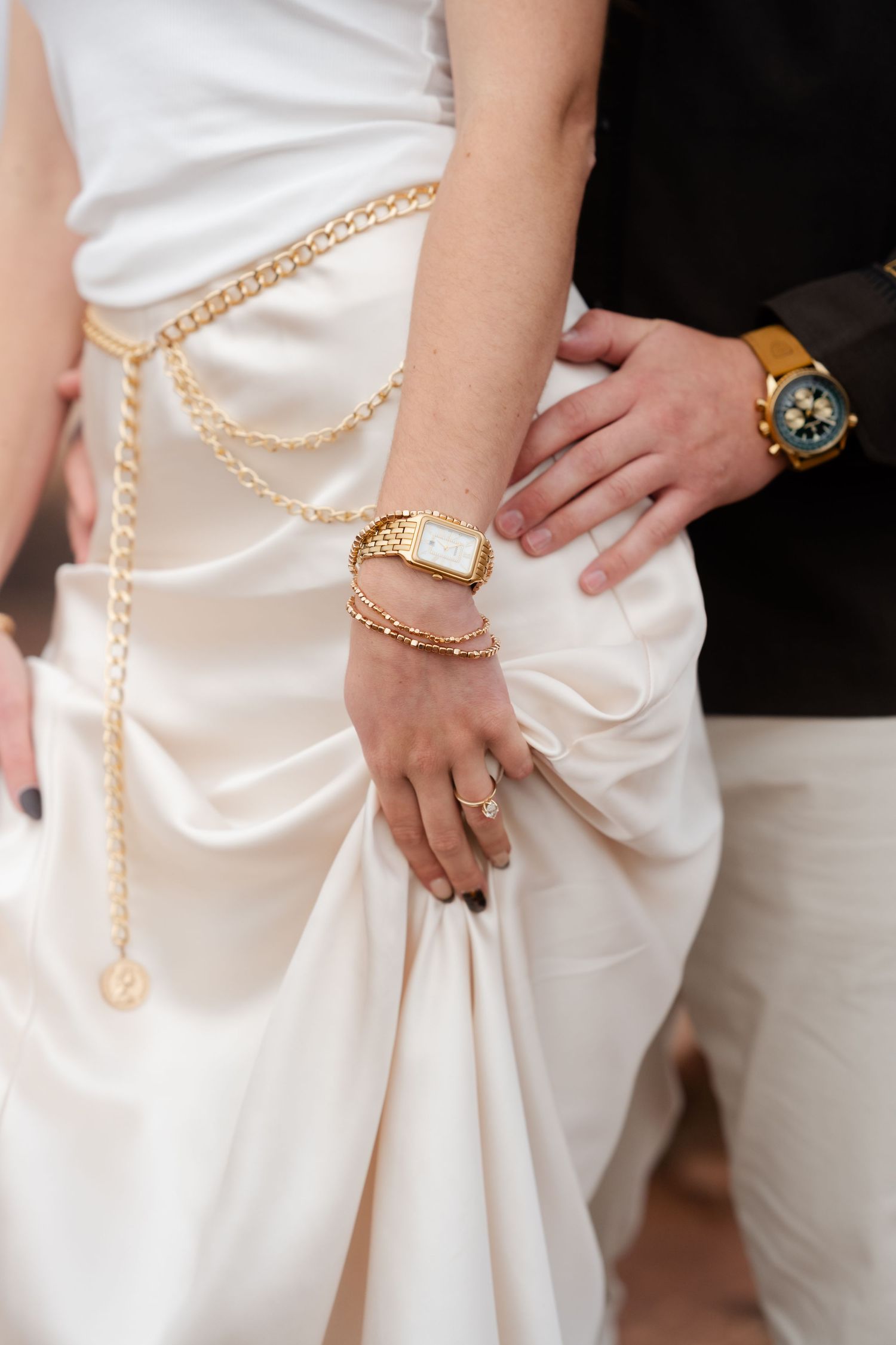 Close-up of elegant white dress with gold chain belt and jewelry accessories against dark background.