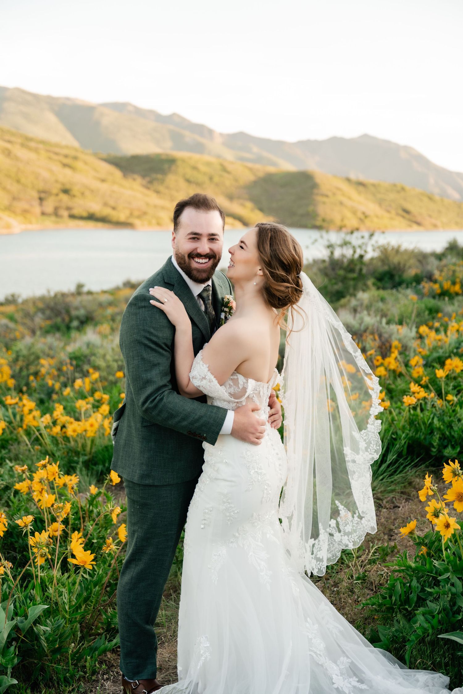 Joyful wedding portraits taken in a scenic mountain meadow with blooming yellow flowers.