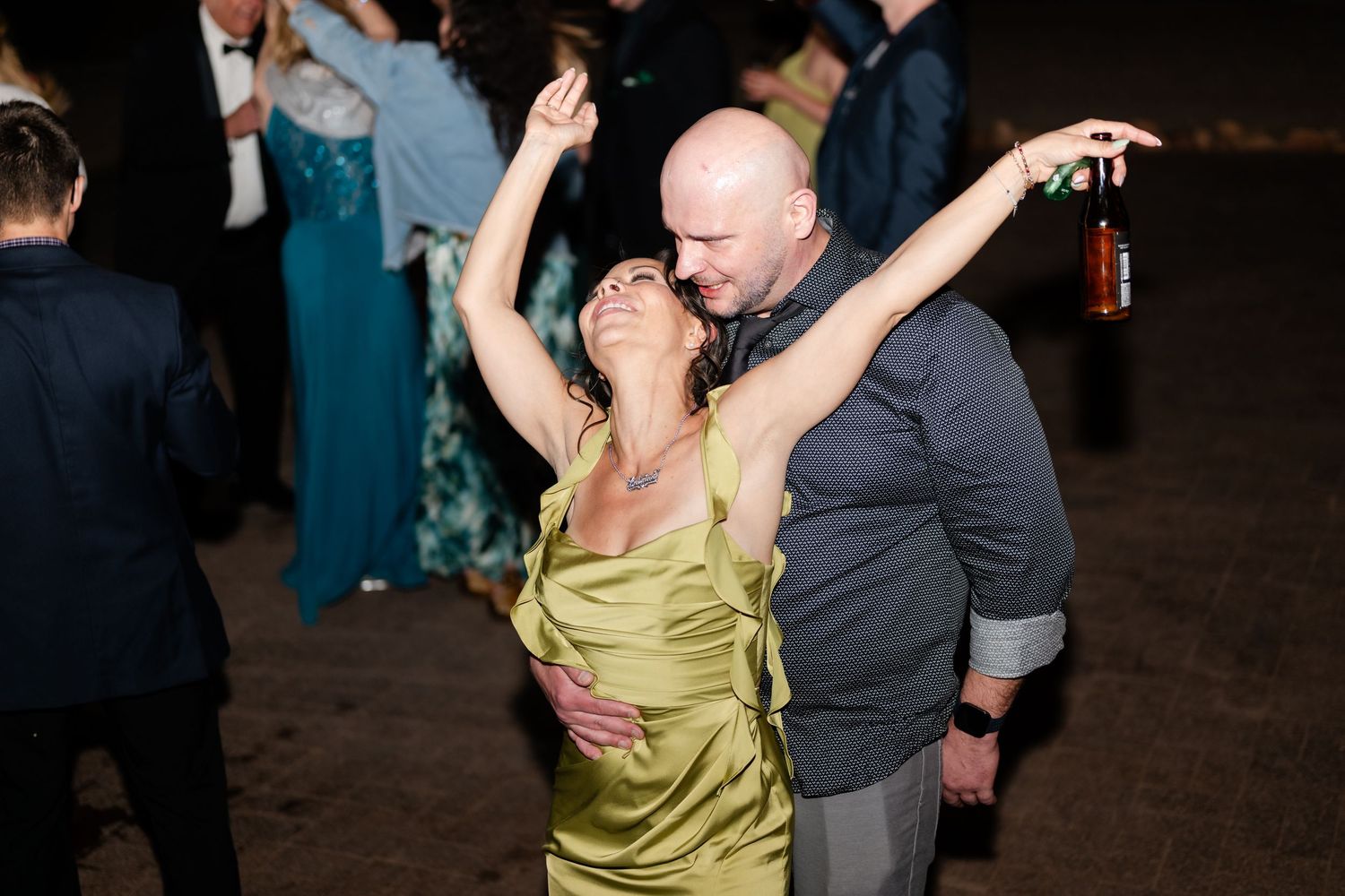 Couple dancing energetically at an outdoor evening wedding reception under the night sky.