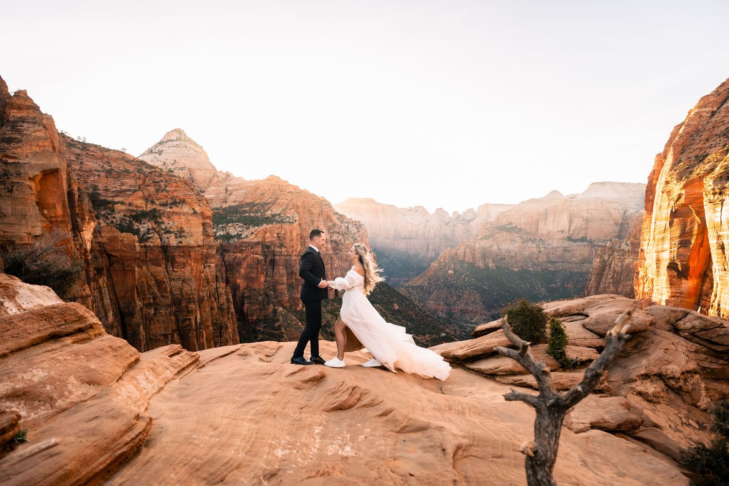 Newlywed couple poses on red rock cliffs at sunset in Zion National Park for romantic wedding photos.