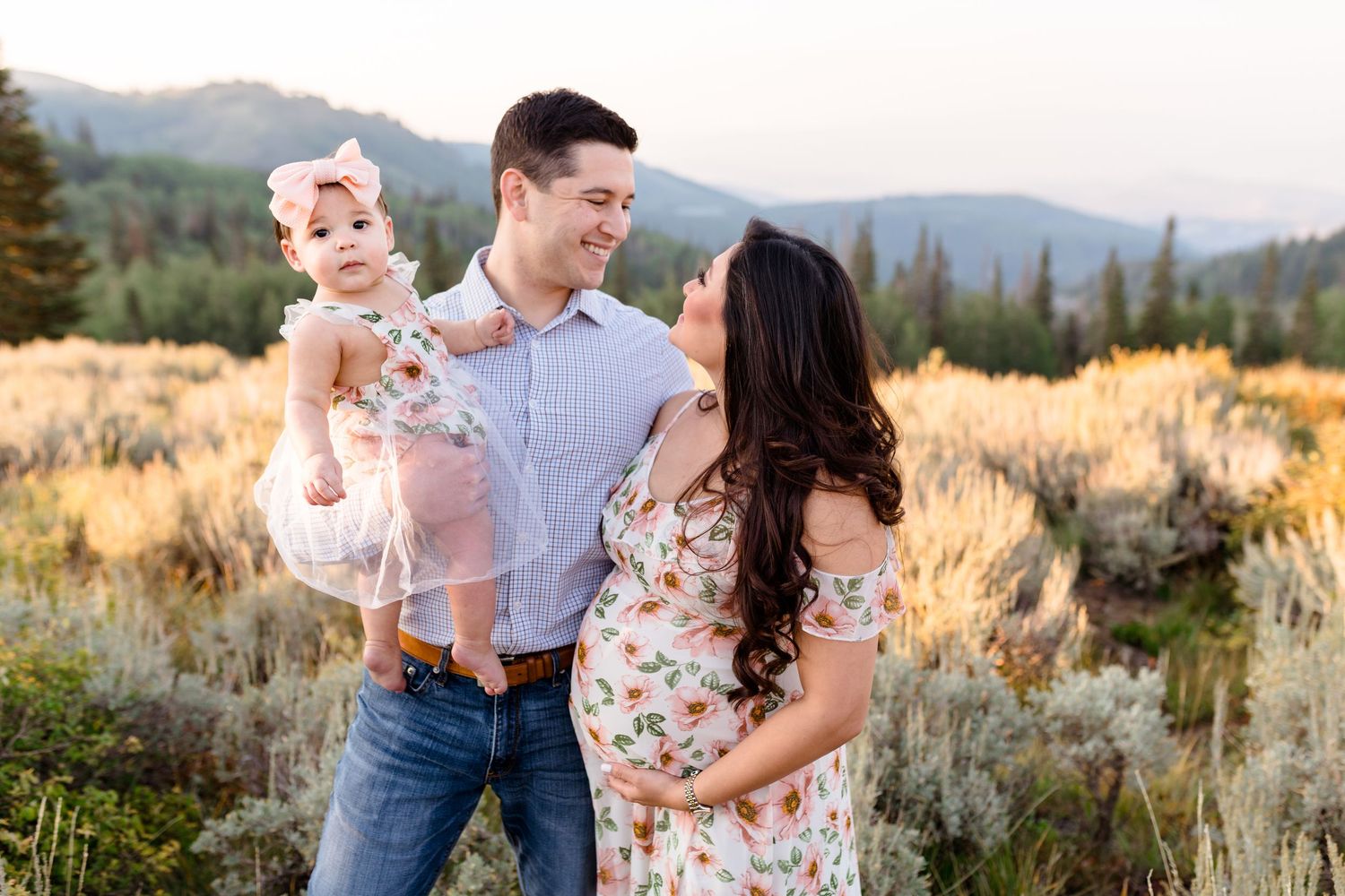 A family stands together in a scenic mountain meadow at sunset among tall sagebrush and golden grasses.