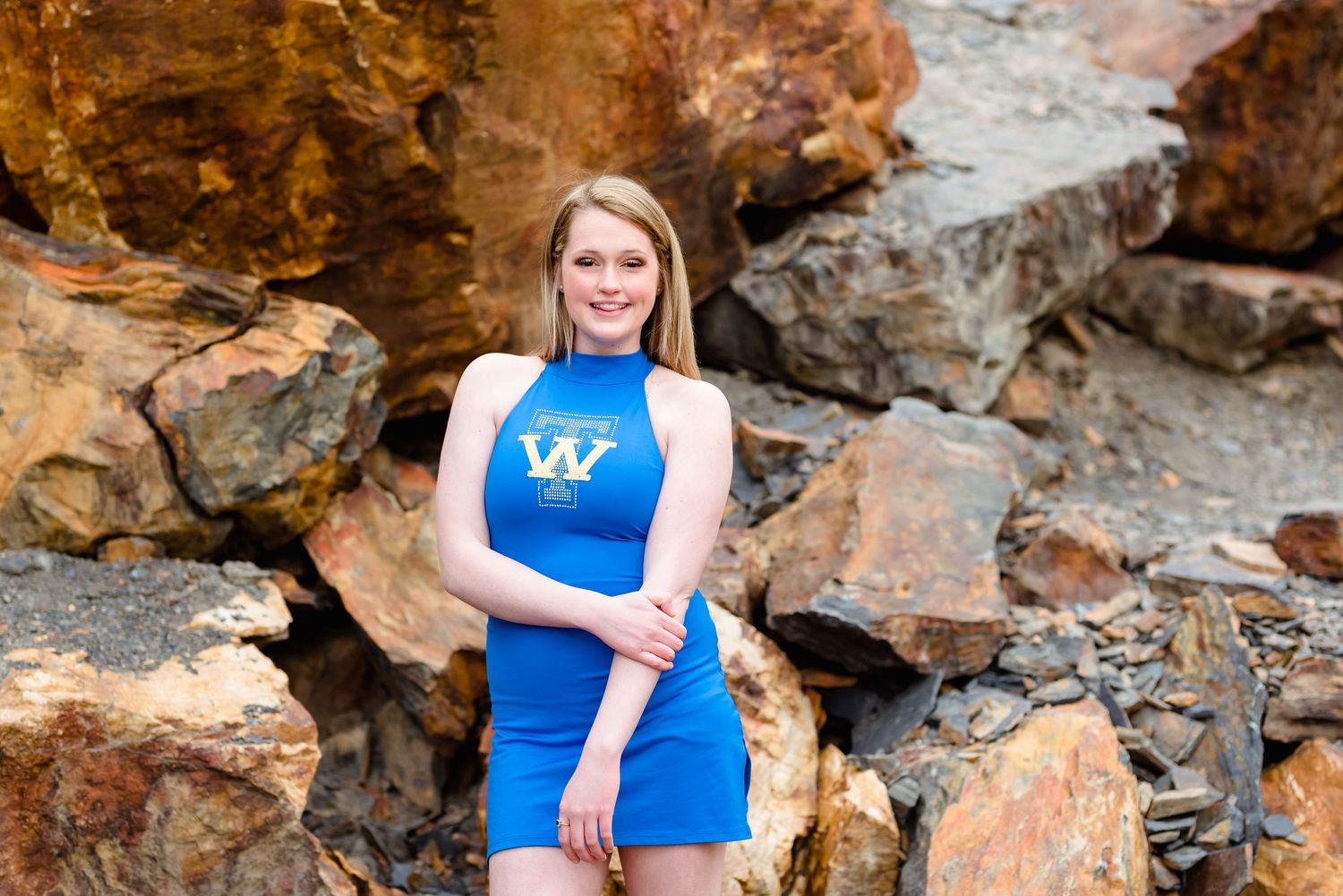A woman in a bright blue dress poses against a rocky cliff background during an outdoor photo session.