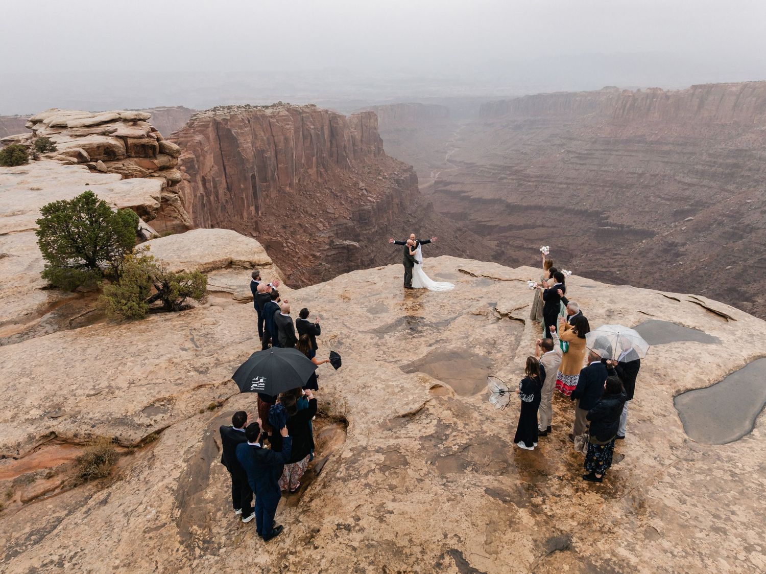 Intimate wedding ceremony taking place on dramatic canyon rim with cloudy skies.