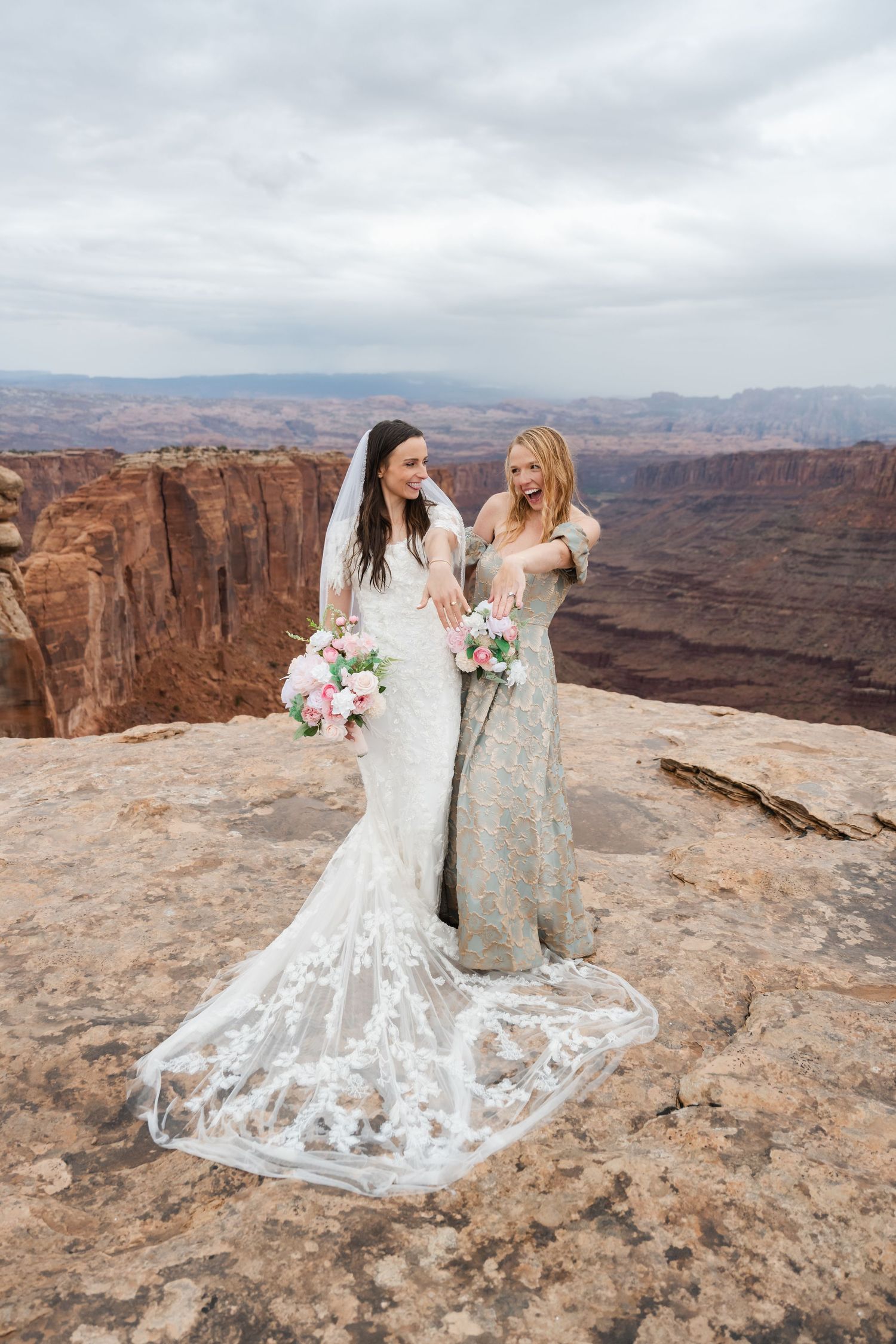 Two people in wedding attire pose together on rocky cliffs overlooking a vast canyon landscape.