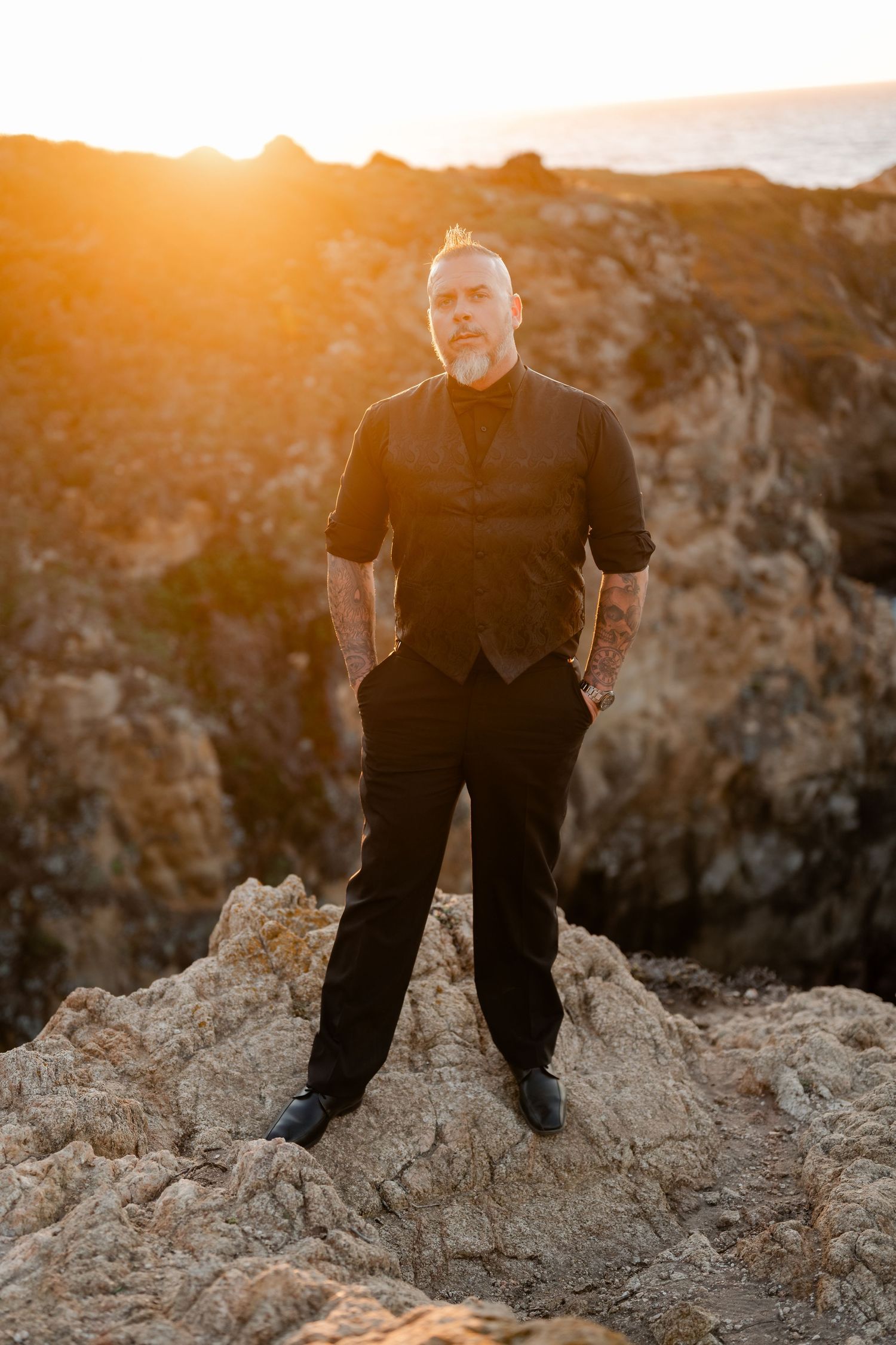 A silhouette of a person standing on coastal rocks during a dramatic sunset.