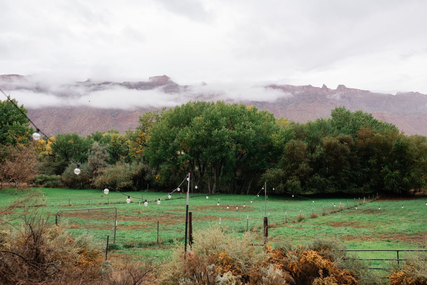 Rolling green countryside with wooden fence posts stretching into the distance under cloudy mountain skies.