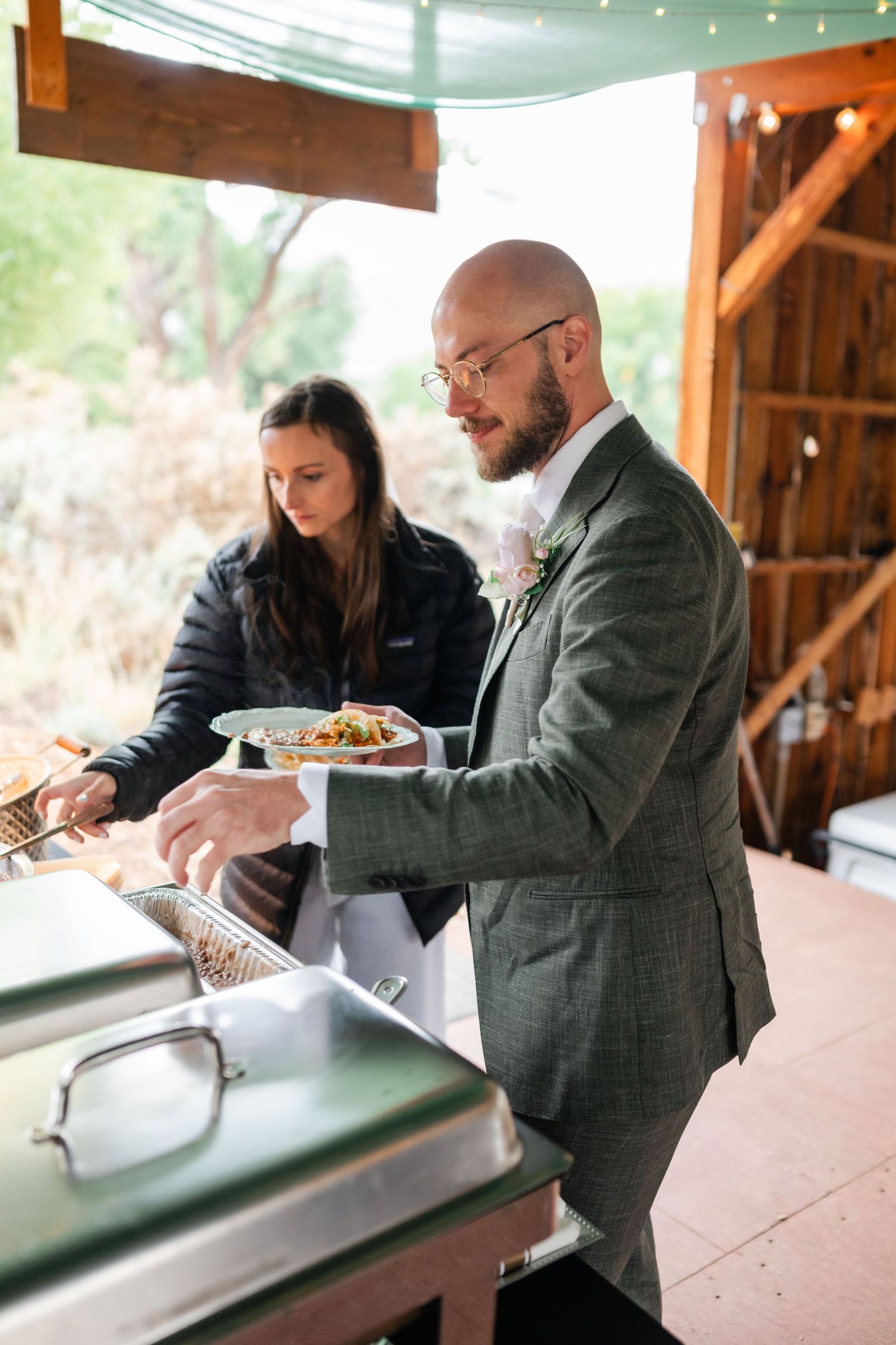 Guests being served food at rustic wooden counter during catered event.