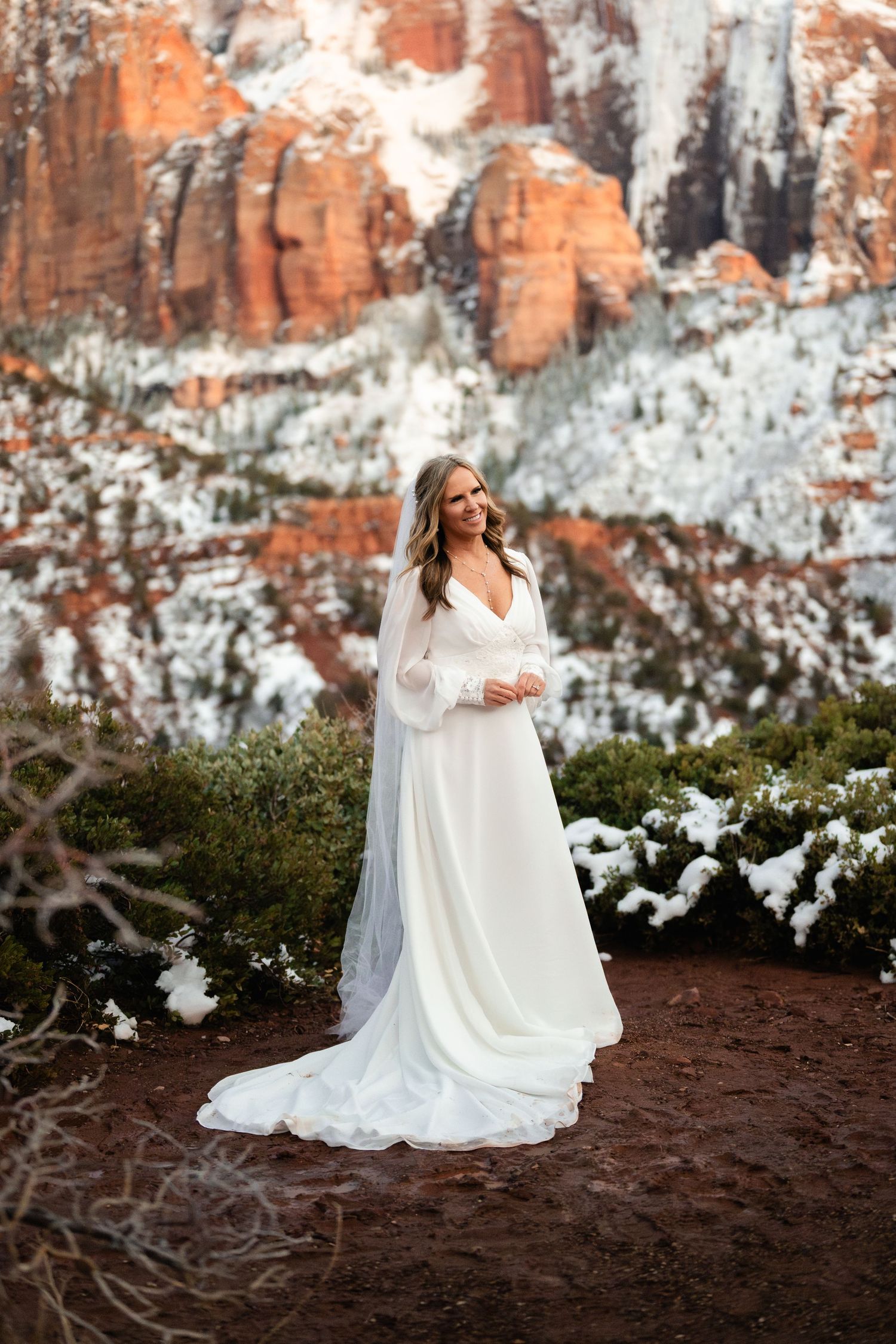 Elegant bridal portraits against snow-covered red rock cliffs with dramatic winter lighting.