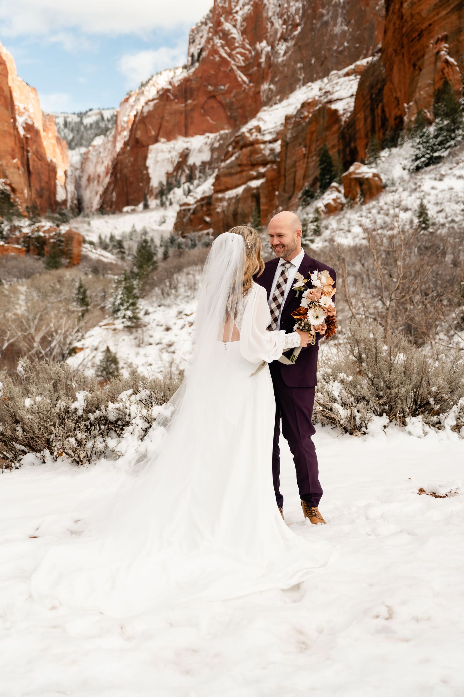 A couple shares an intimate moment in their wedding attire surrounded by snow-covered red rock formations.