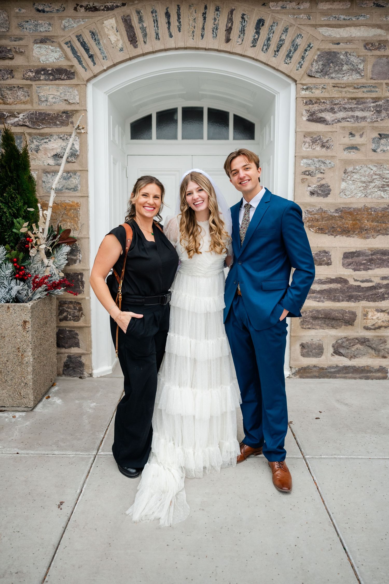 A wedding party poses in front of a stone wall with arched doorways in a series of playful group photos. LDS Logan Temple wedding.