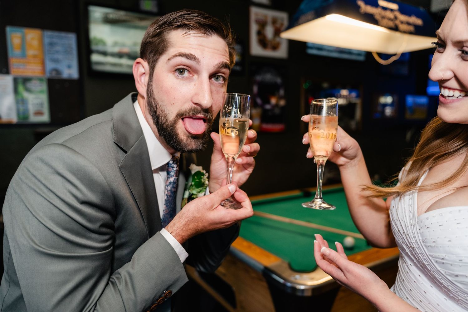 A couple shares a playful moment while toasting with champagne glasses at a celebration event.