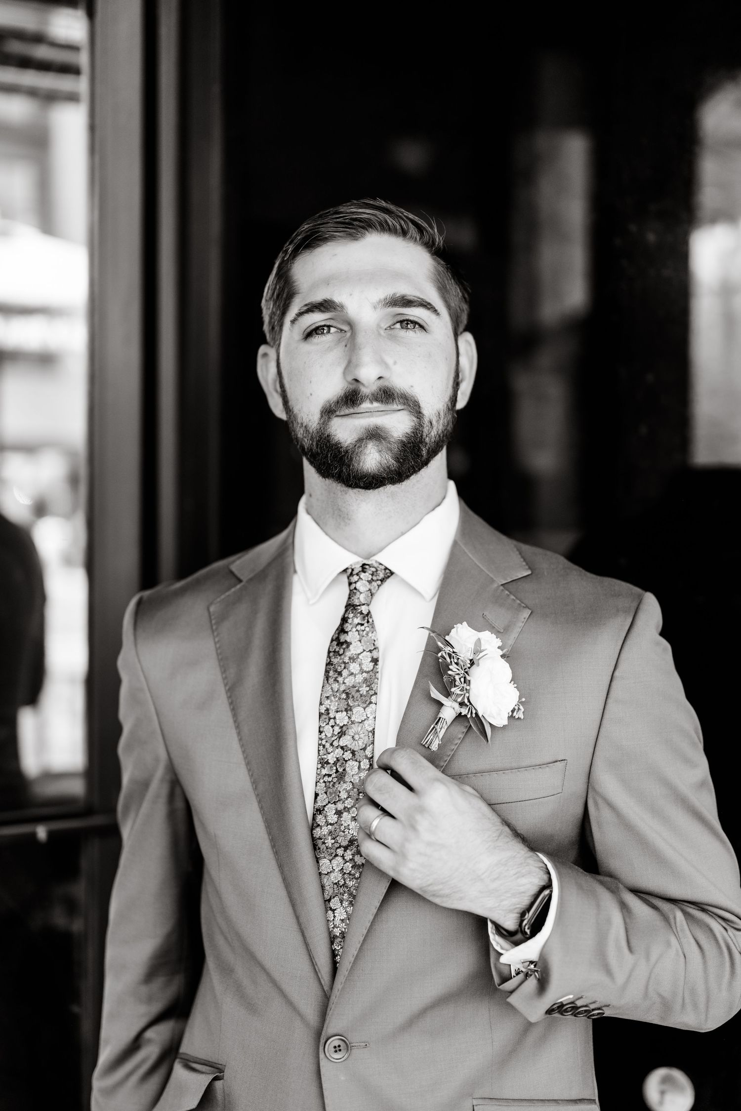 Groom in gray suit with floral tie and boutonniere adjusting jacket.