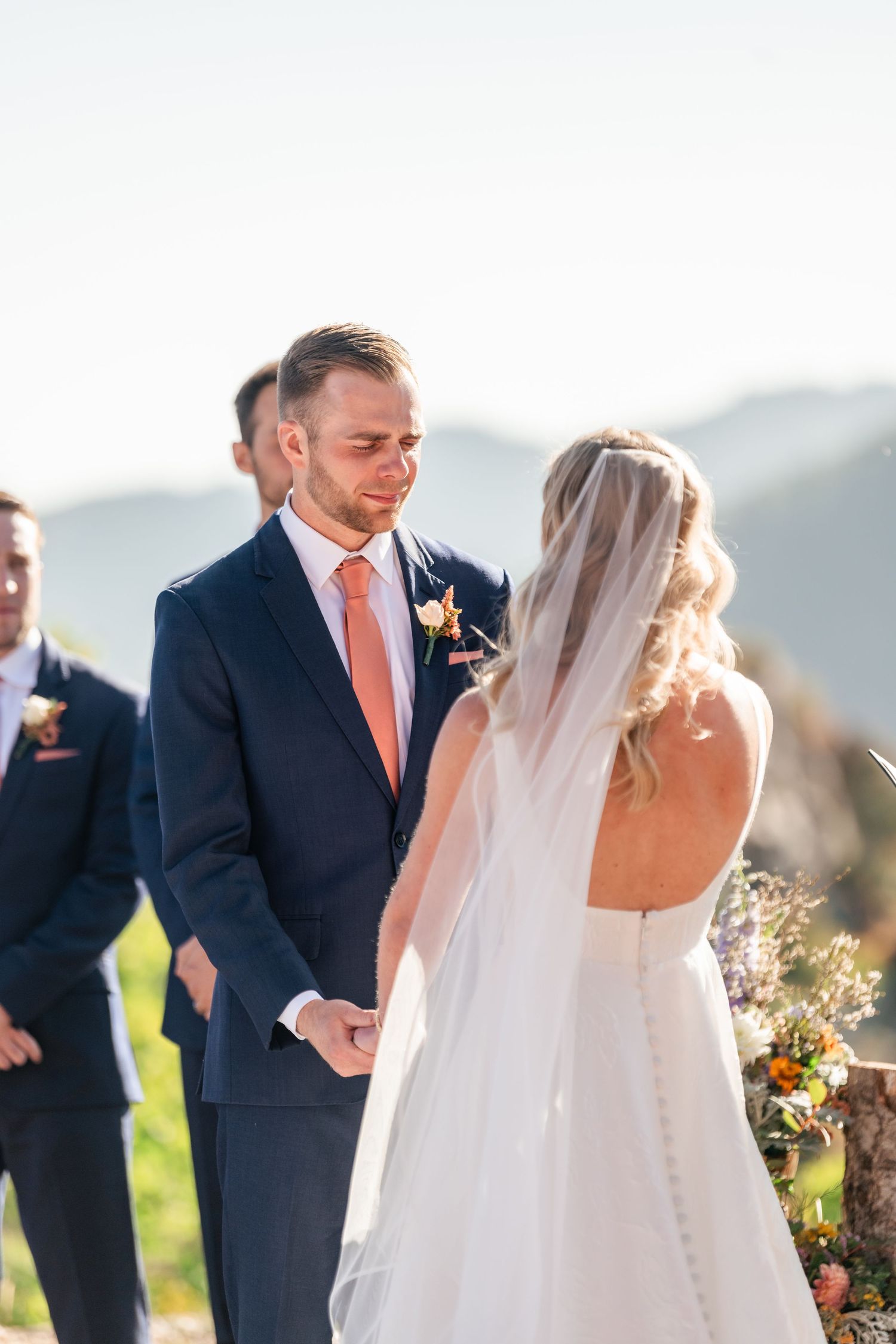 Wedding ceremony taking place outdoors with mountains and sunlight in background.
