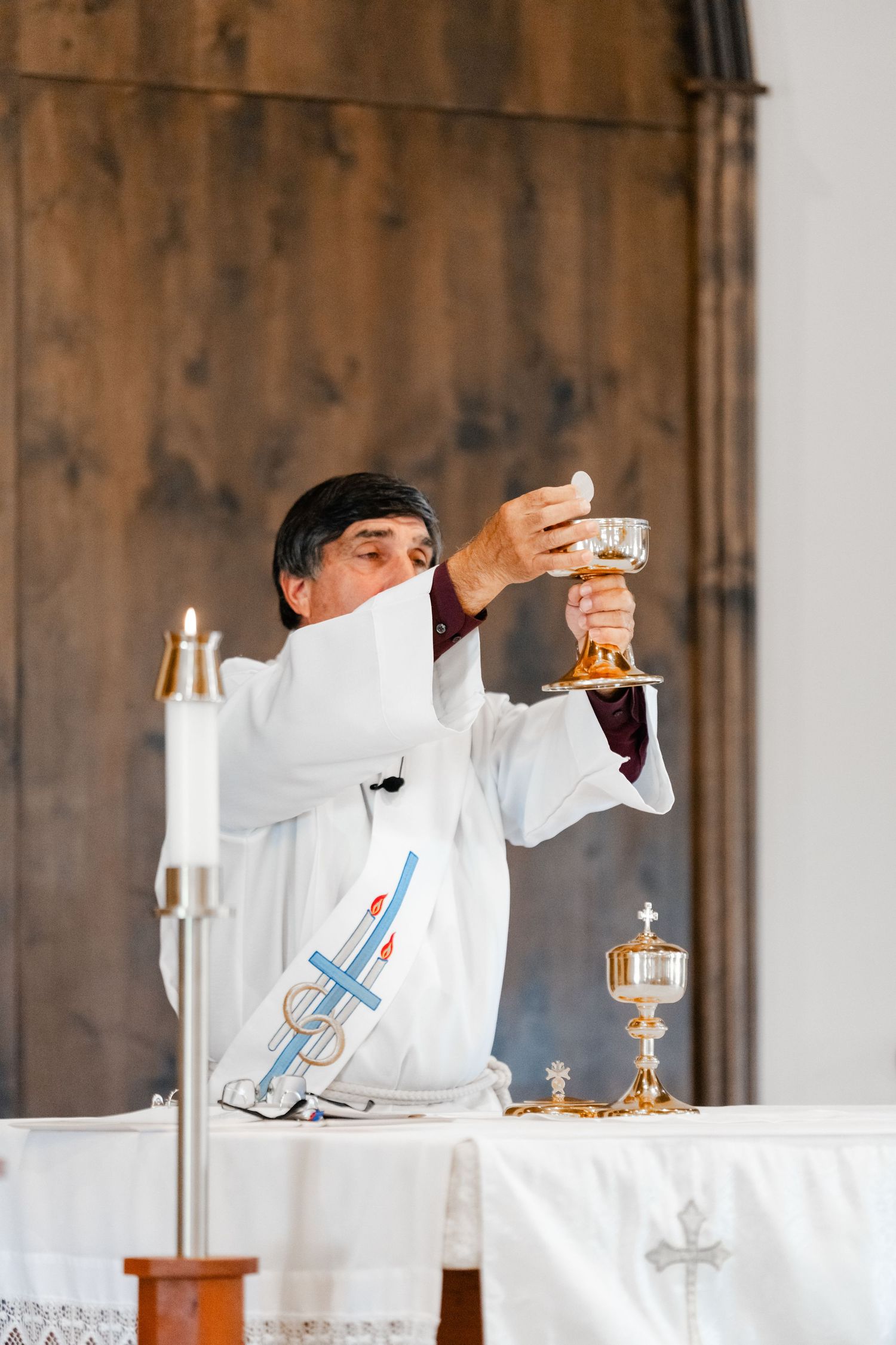 Person in white robe performing communion ritual at church altar.