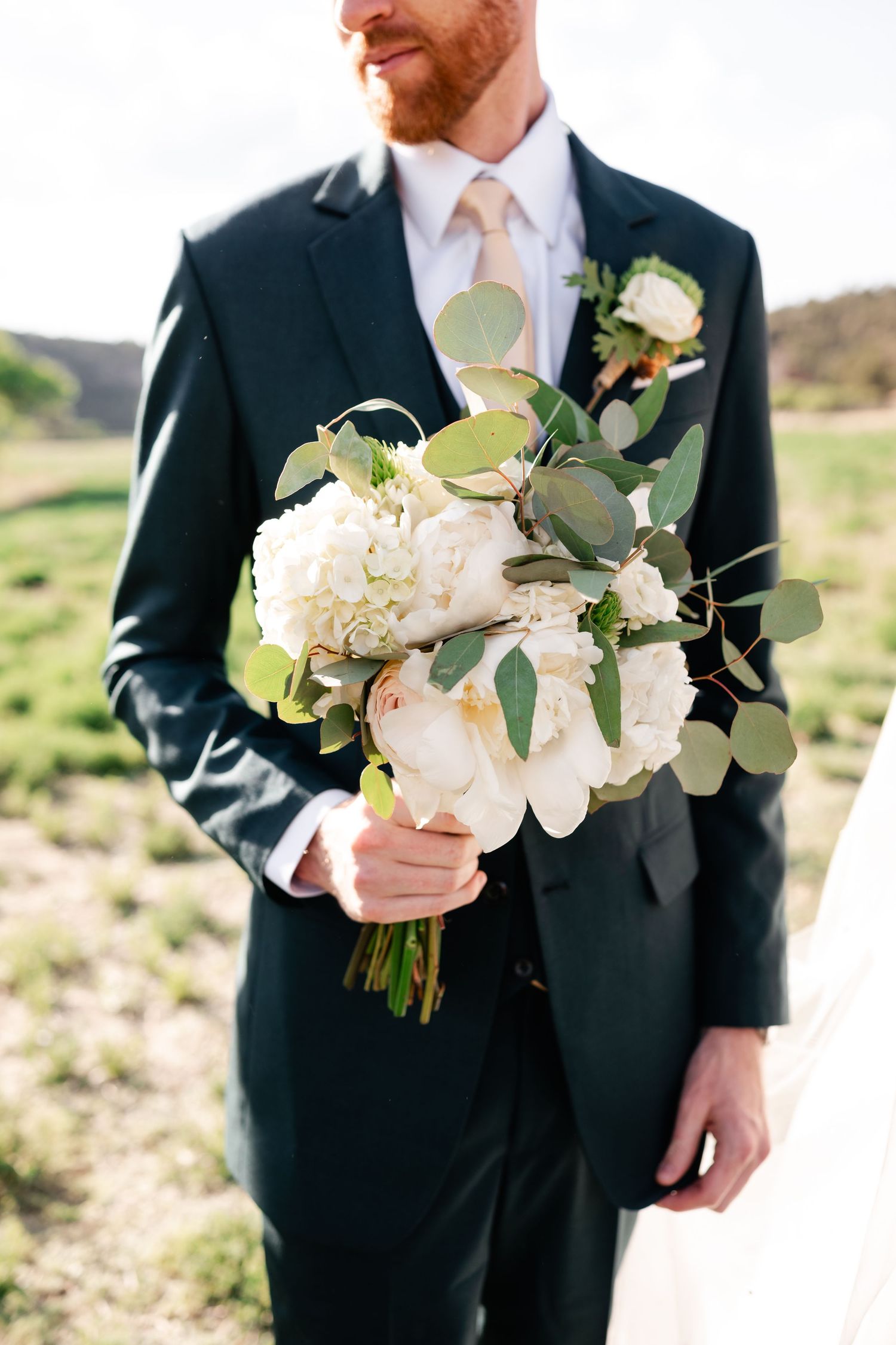 Wedding bouquet with white flowers and eucalyptus held by groom in dark suit.