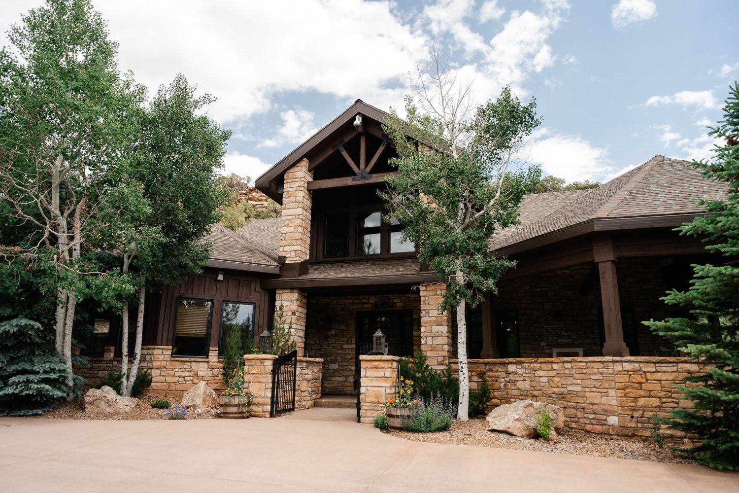 A rustic stone and wood lodge with multiple buildings nestled among trees under a blue summer sky.