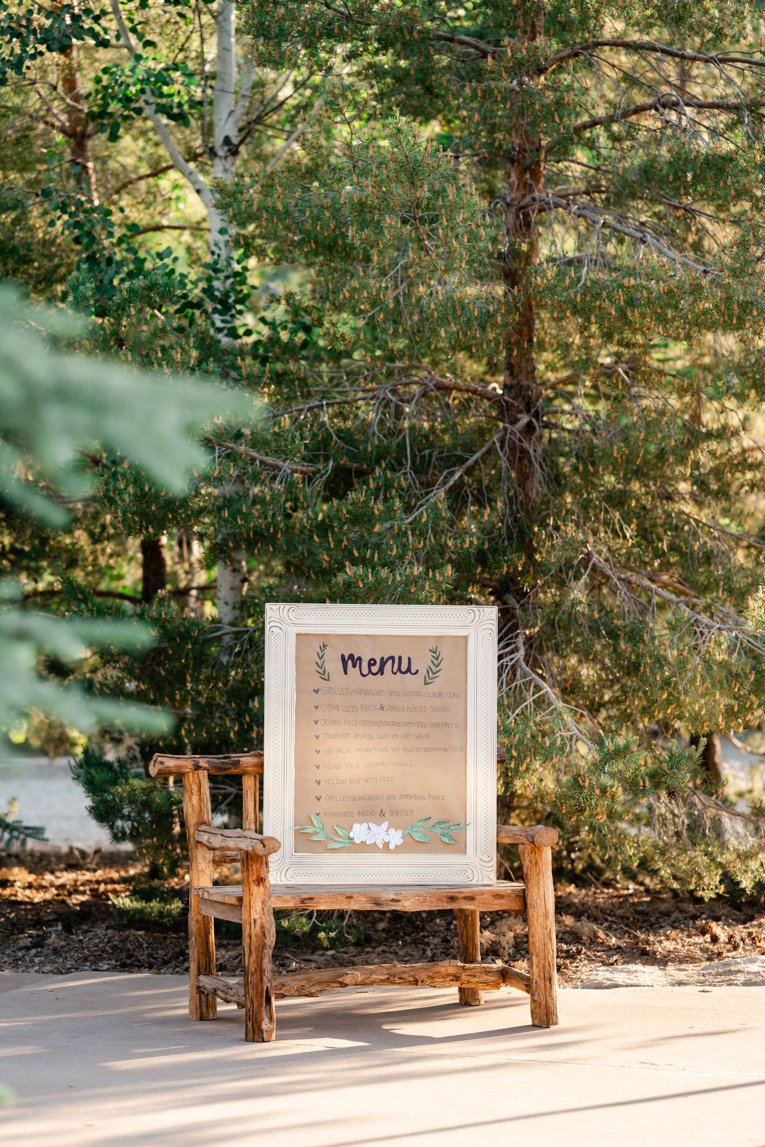 A wooden menu sign display on a rustic chair against a forest backdrop.