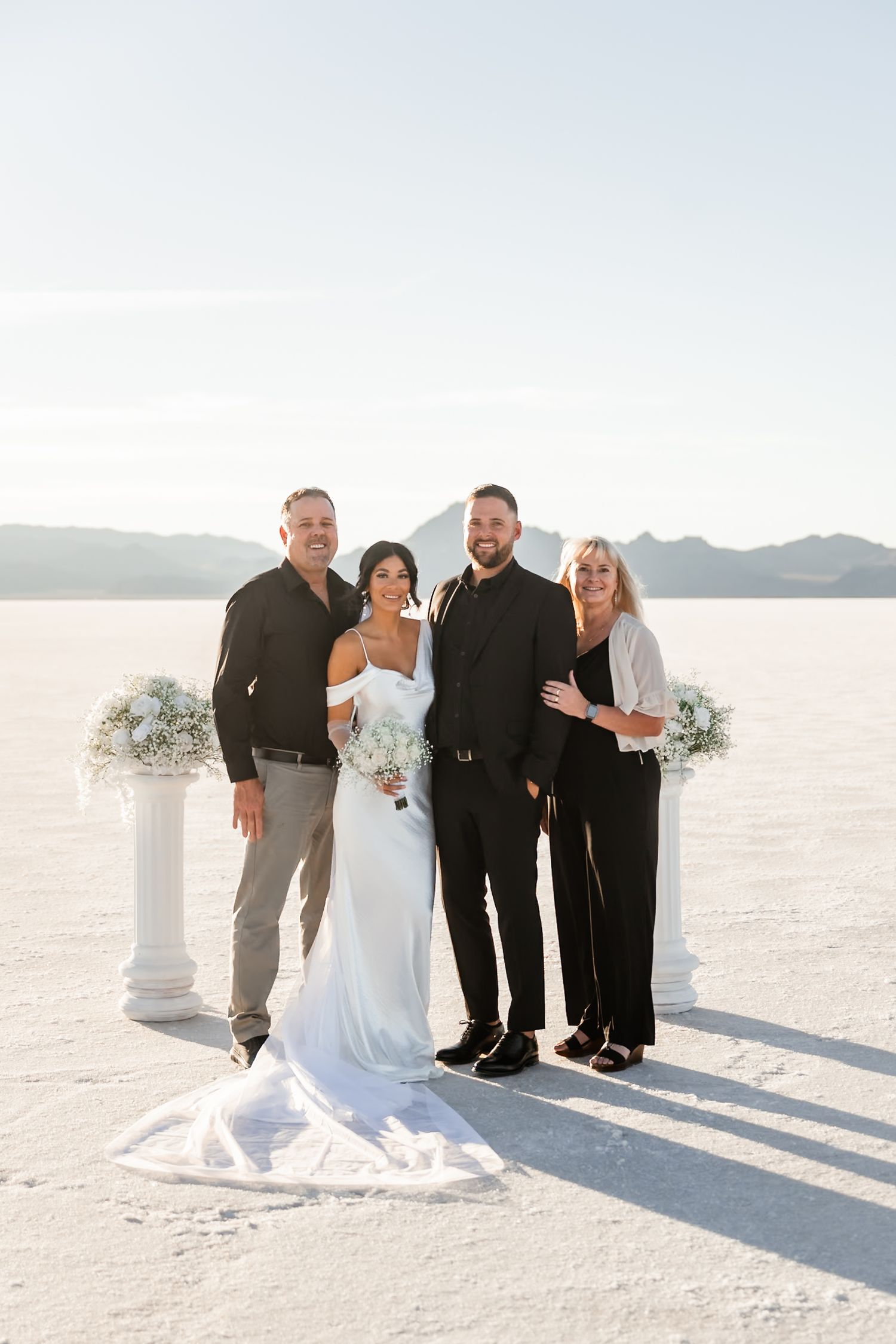 Wedding group stands together against a mountain backdrop on white salt flats.