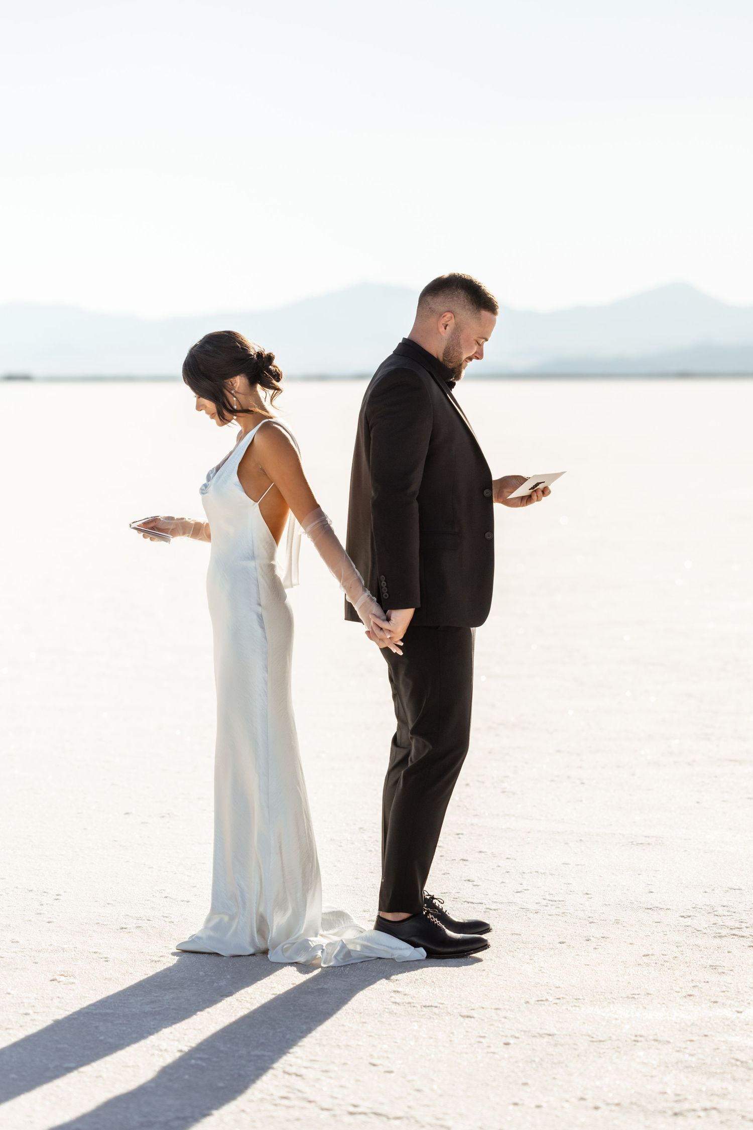 Wedding couple standing back-to-back on white salt flats under blue sky.
