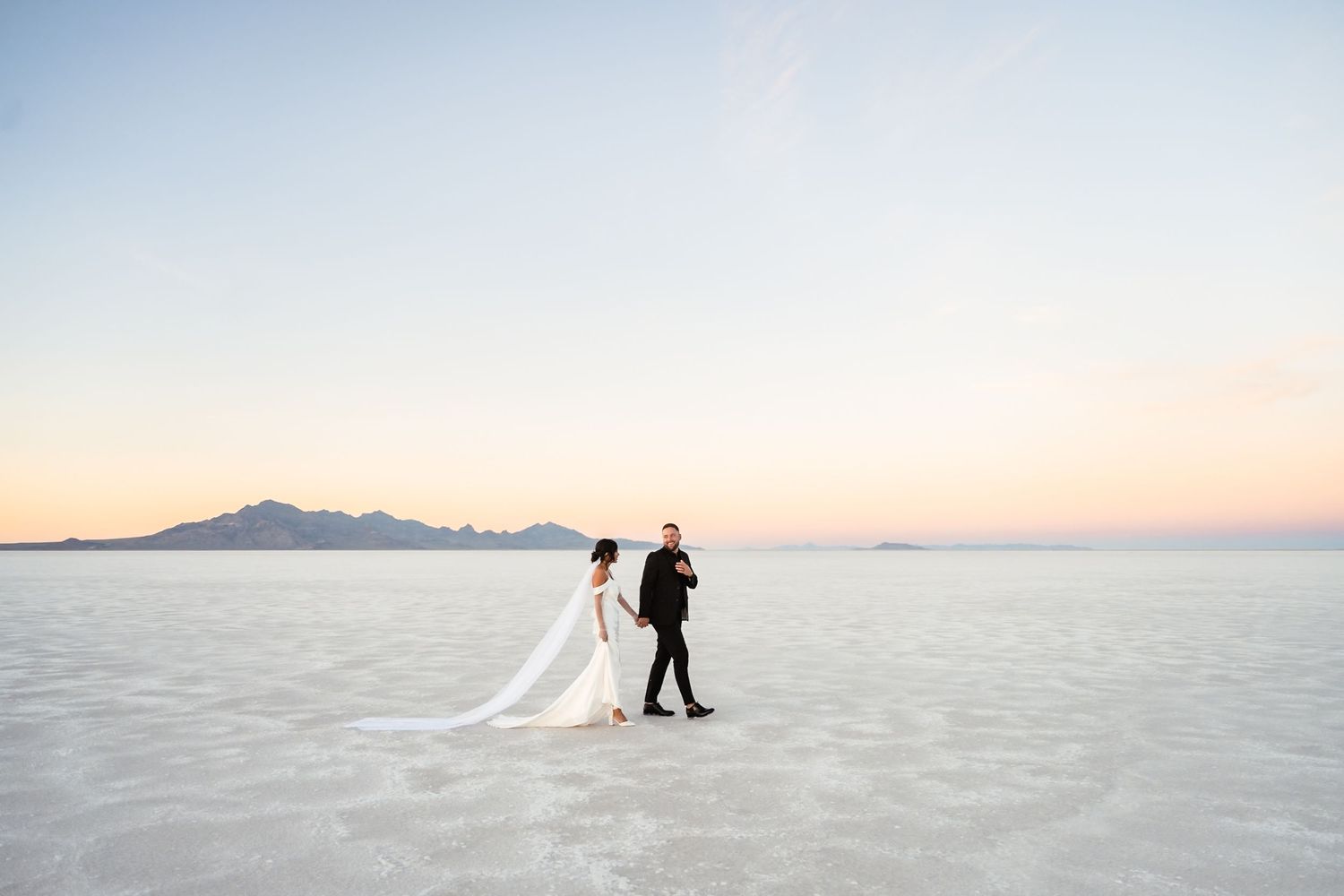 Minimalist wedding photography on salt flats with distant mountain silhouettes at dusk.