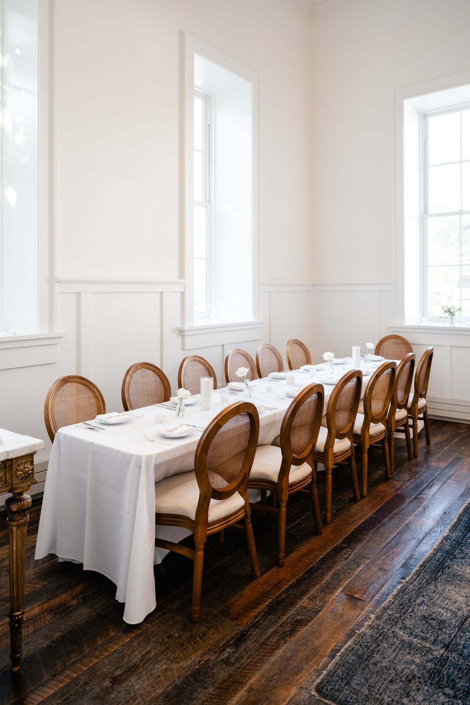 An elegant dining room with wooden chairs and white tablecloths arranged in rows.