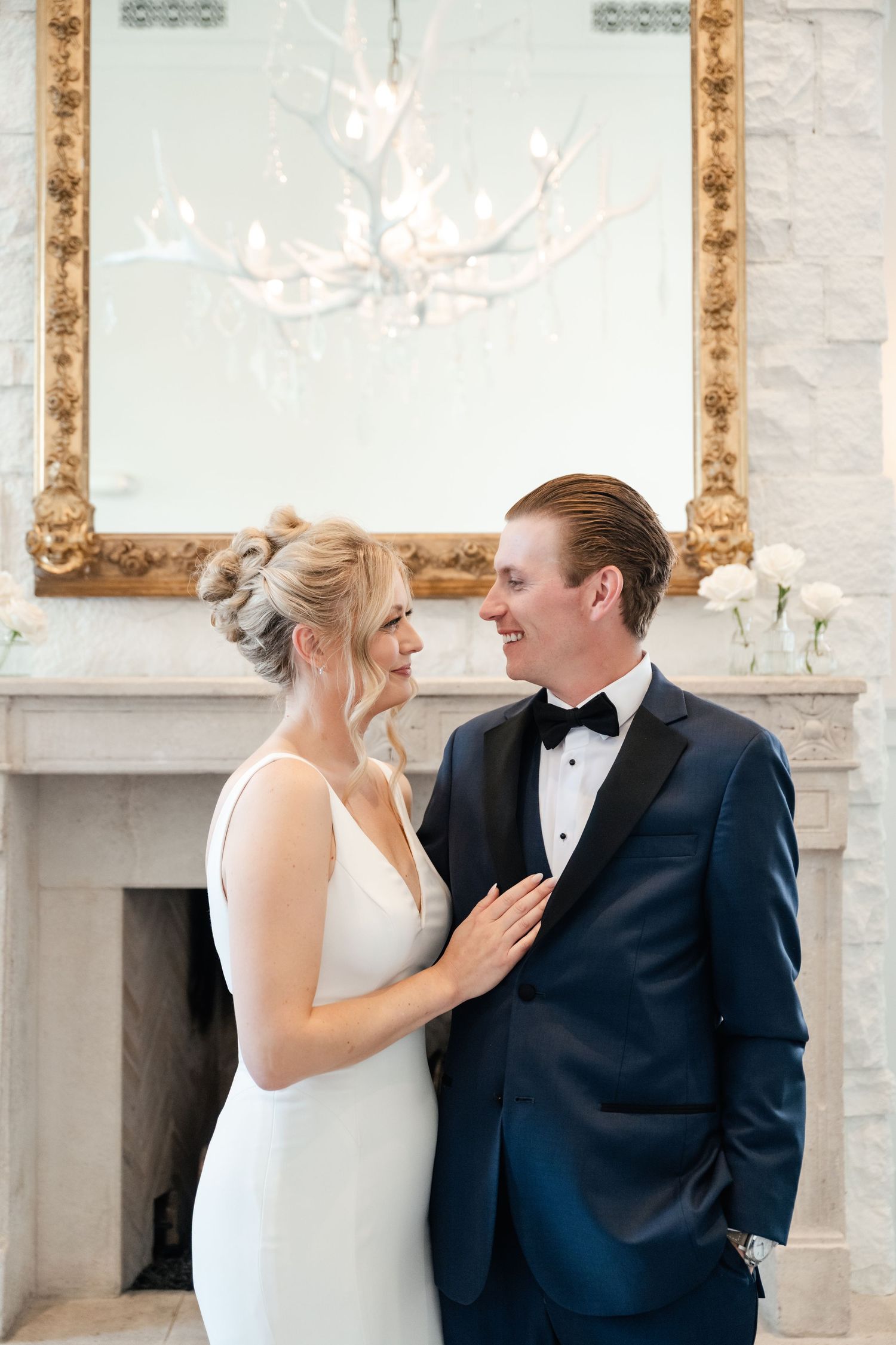 Bride and groom share a romantic first look moment in an elegant white room with ornate gold-framed mirrors.