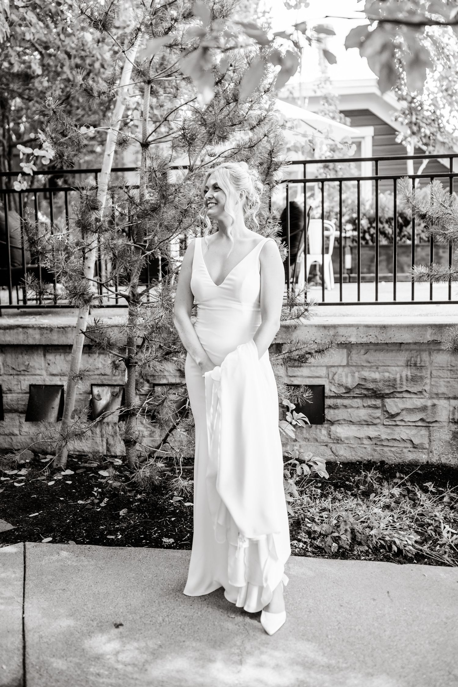 Black and white portrait of bride walking along stone patio with iron railings.