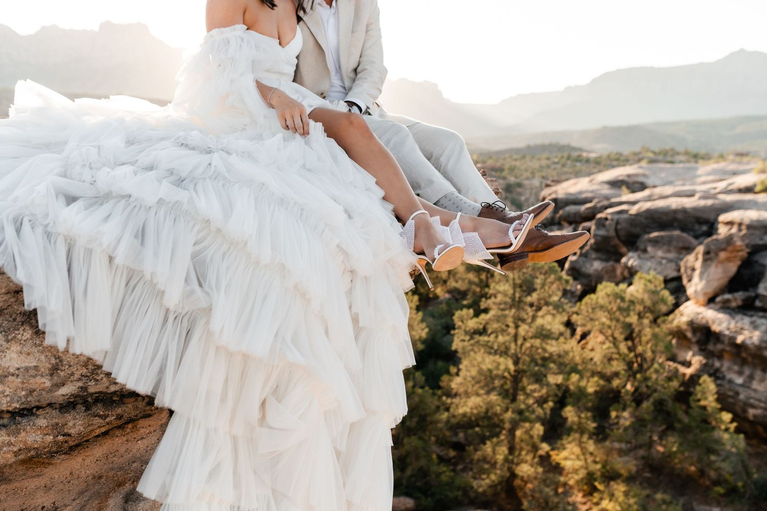Zion Adventure Session. Wedding couple standing on rocky cliff edge with flowing white dress in desert landscape.