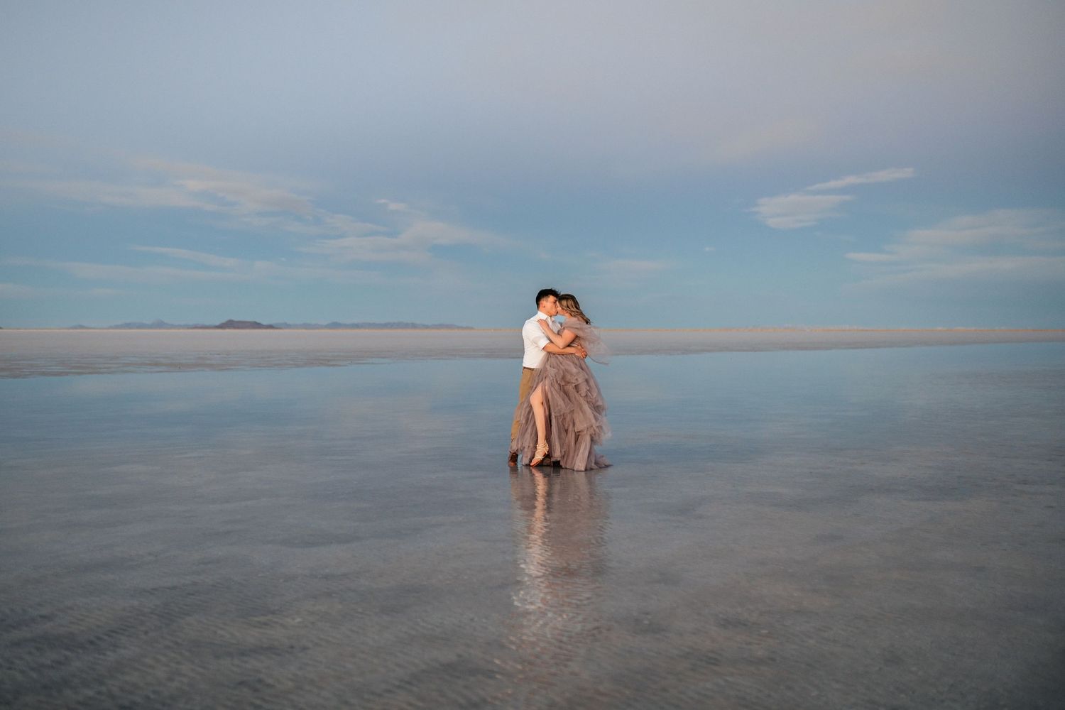 Romantic moment captured as the couple embraces amidst the serene beauty of the flooded Salt Flats during blue hour