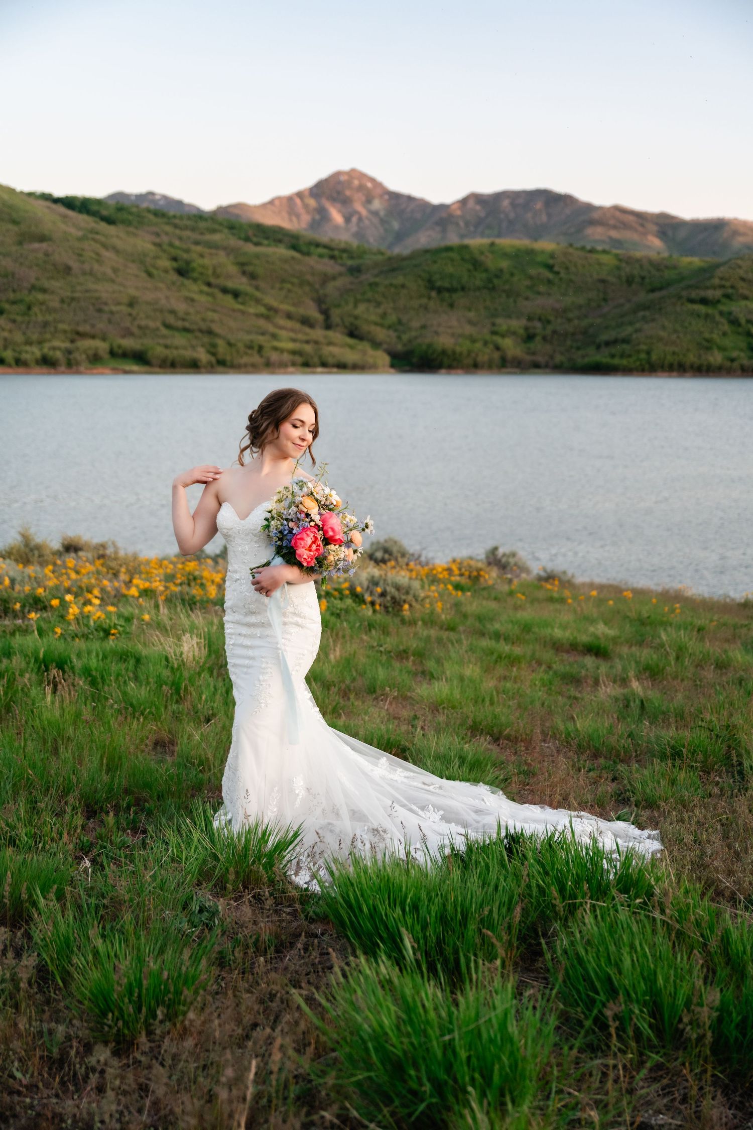 Wedding photos by a lake with mountain backdrop showing bride in lace dress among spring wildflowers.