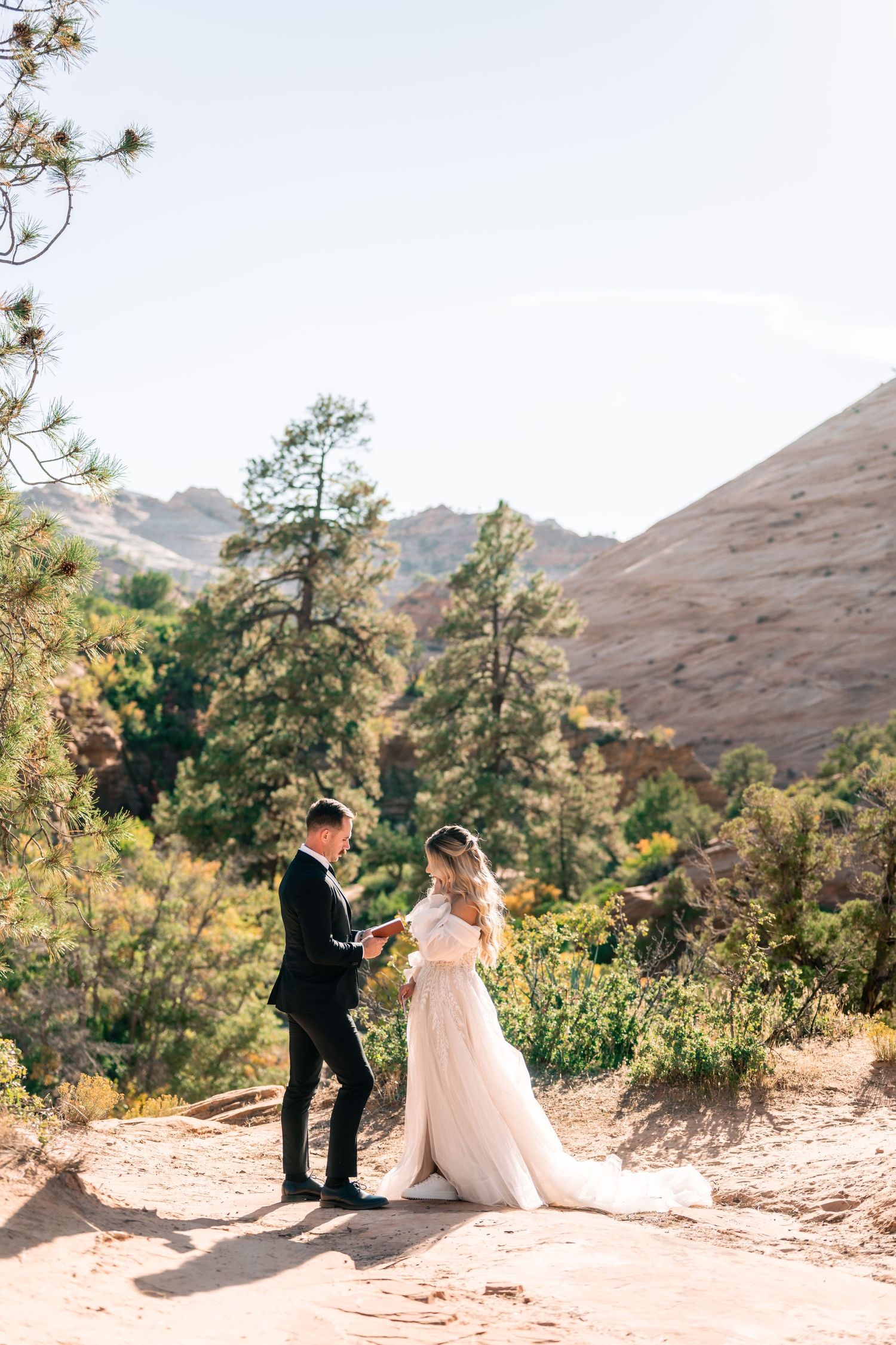 Newlyweds exchange vows on a scenic mountain trail with red rock formations in the background.